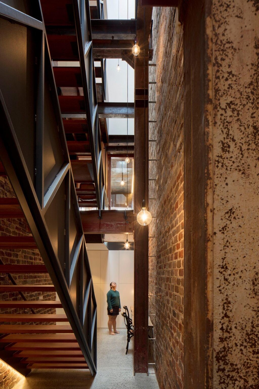 A dramatic four-storey brick wall runs alongside a skylit staircase, with exposed steel beams and a 12-metre void bringing natural light deep into this Sydney warehouse conversion.