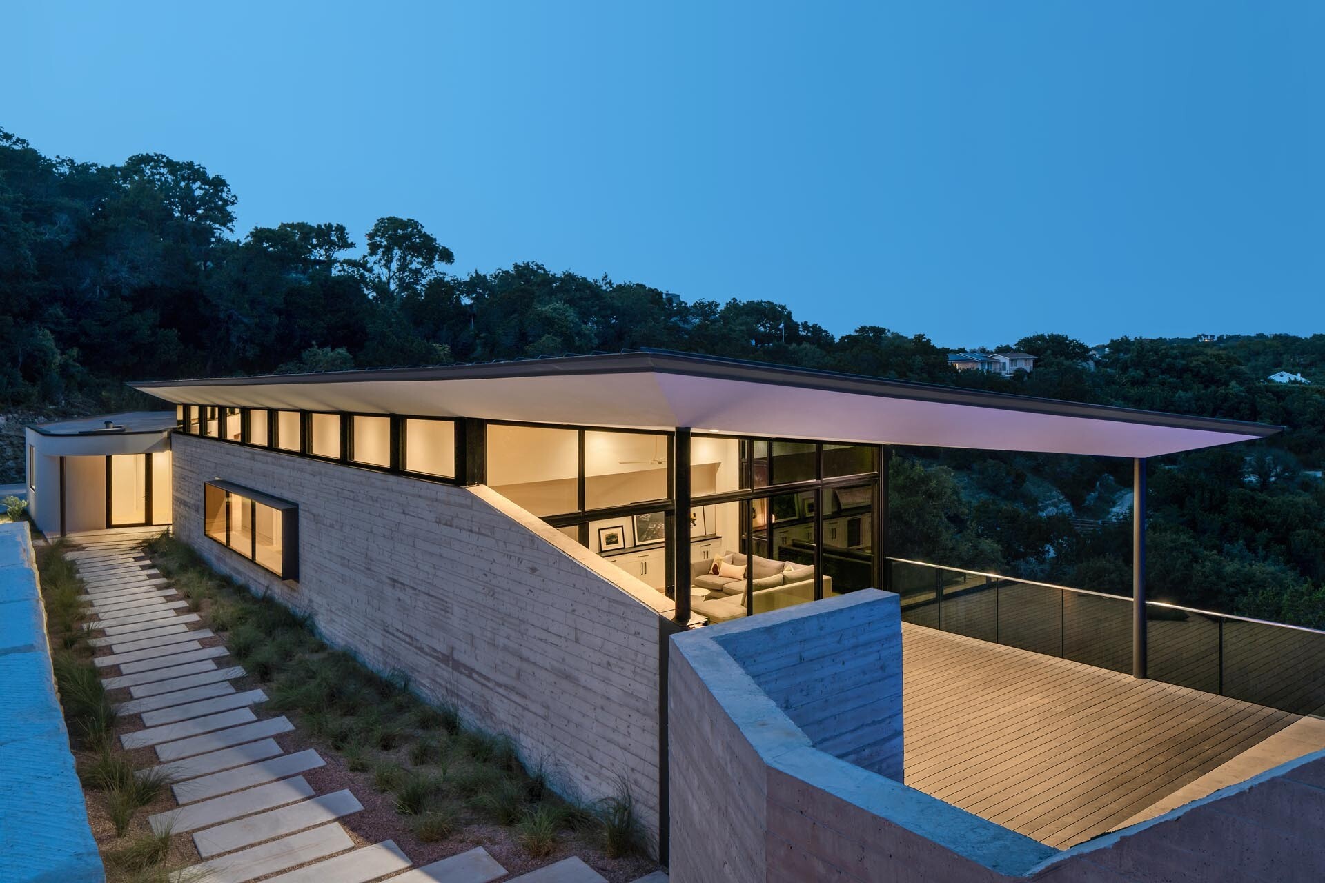 Board-formed concrete walls, grasses, and warm wood details shape the entrance to this modern Austin home.