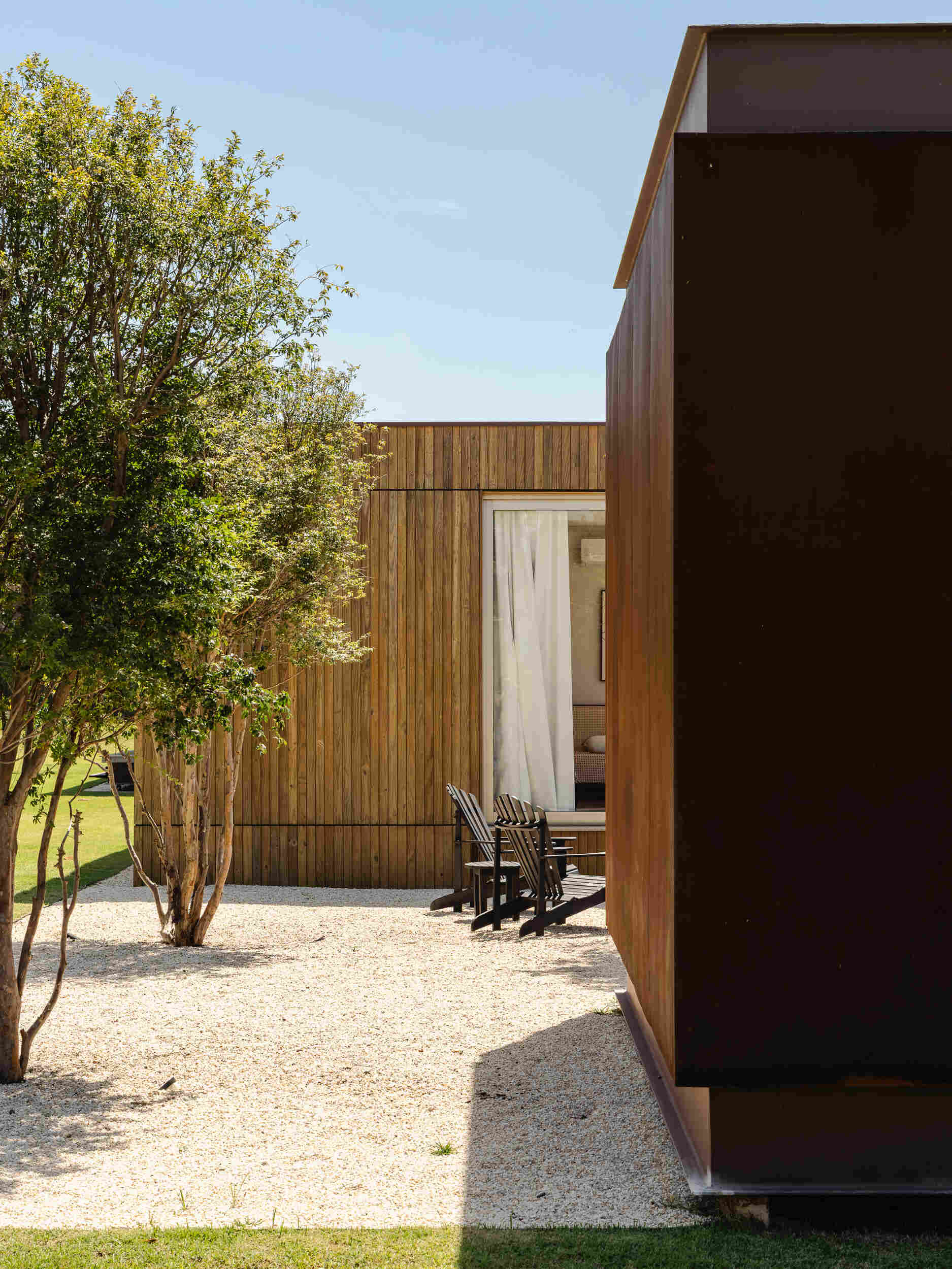 Stone walls, vertical timber slats, and lightweight steel construction give Casa Themis a warm contemporary look while helping the home blend naturally into the Brazilian landscape.