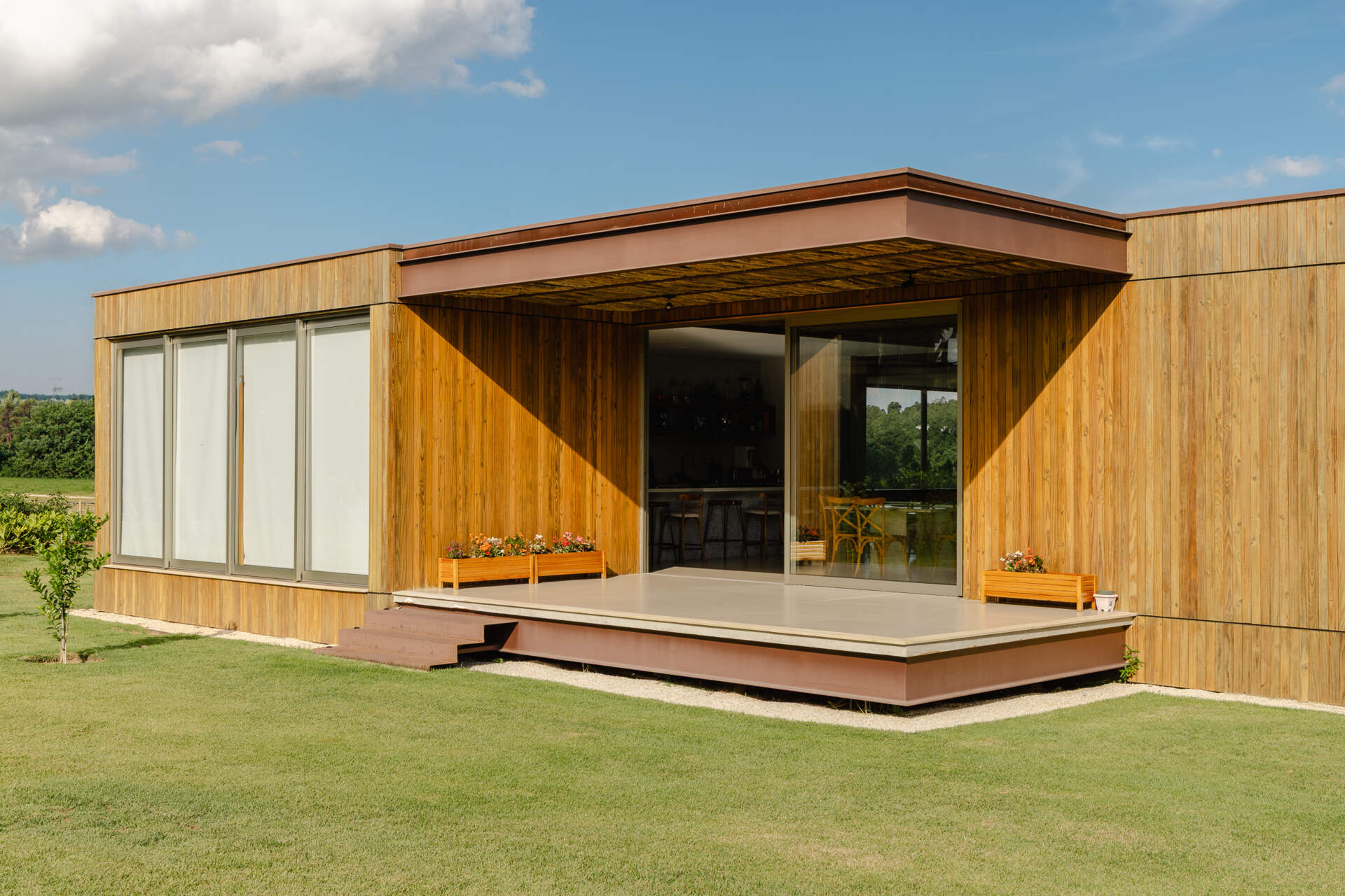 Stone walls, vertical timber slats, and lightweight steel construction give Casa Themis a warm contemporary look while helping the home blend naturally into the Brazilian landscape.