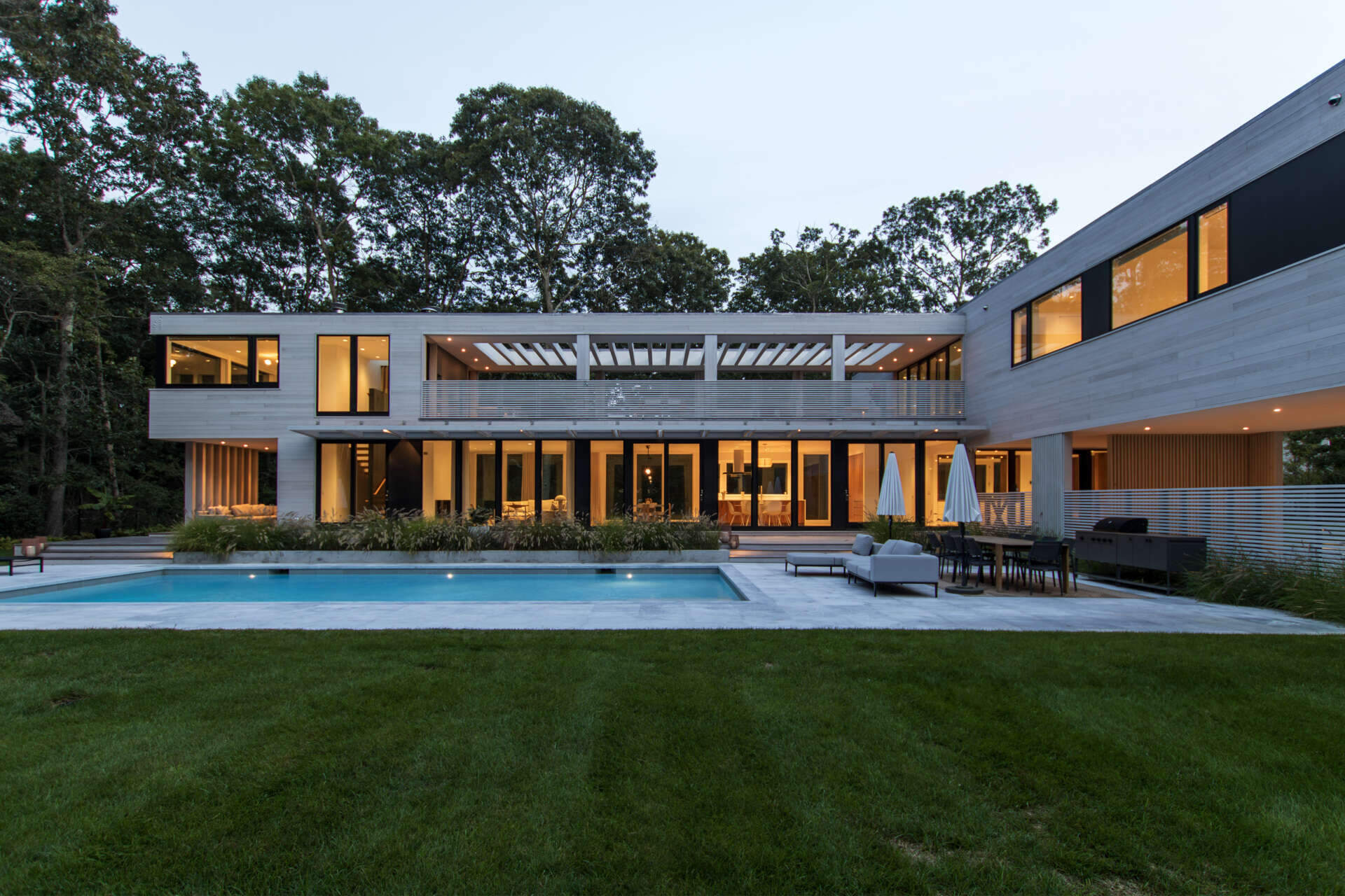 This modular East Hampton home combines bleached cedar siding, expansive glazing, and custom sun screens within a wooded setting.
