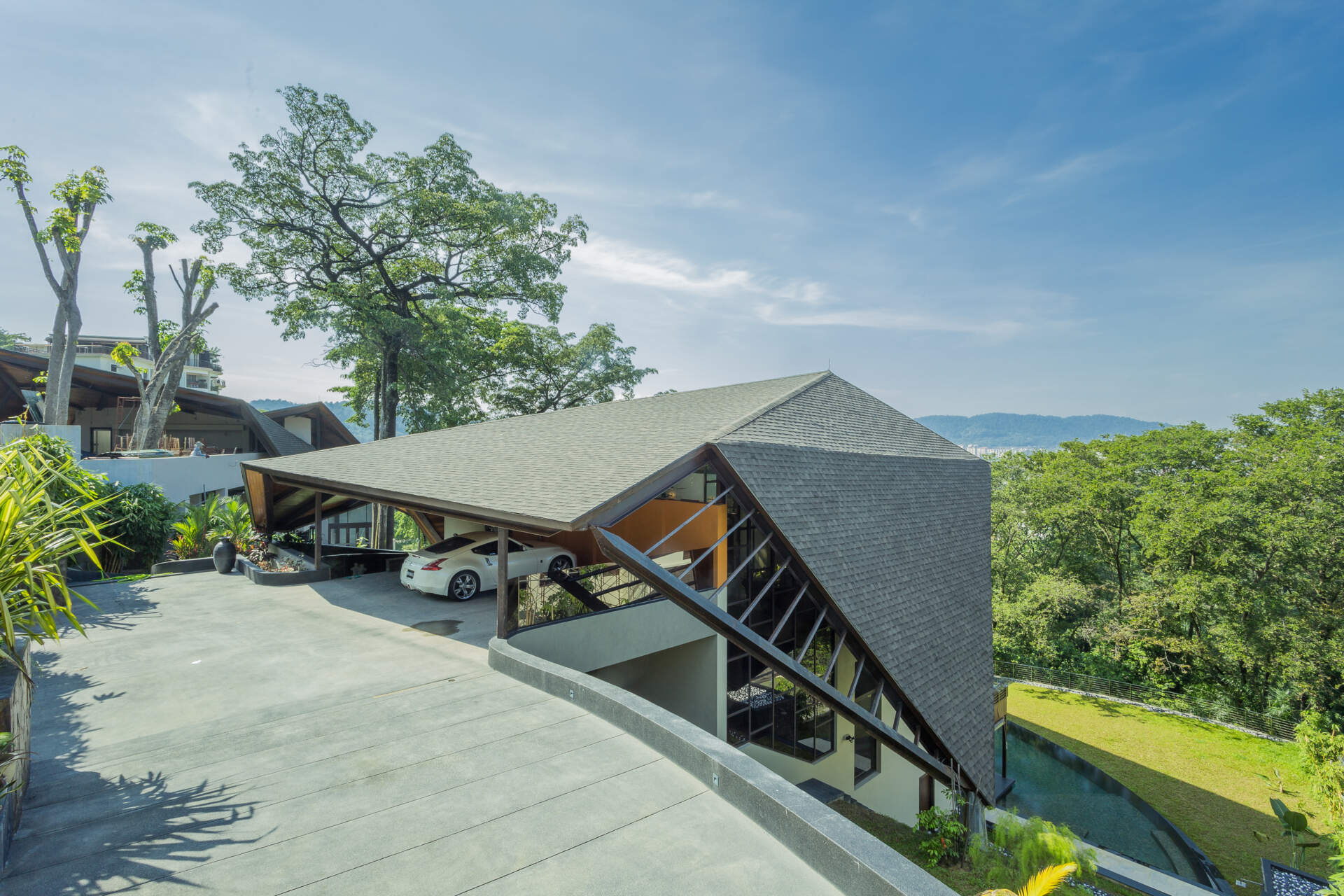A dramatic hillside home in Kuala Lumpur designed by MJ Kanny Architect, featuring a floating timber-lined canopy roof, exposed steel beams and jungle-inspired architecture cascading down a steep slope.