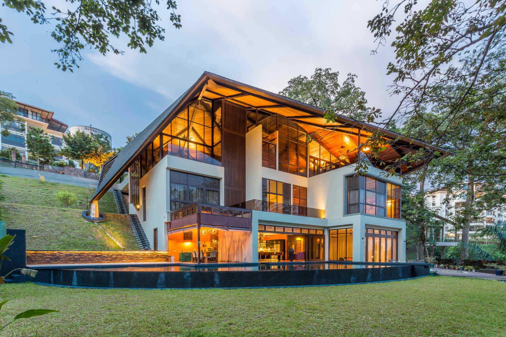 A dramatic hillside home in Kuala Lumpur designed by MJ Kanny Architect, featuring a floating timber-lined canopy roof, exposed steel beams and jungle-inspired architecture cascading down a steep slope.