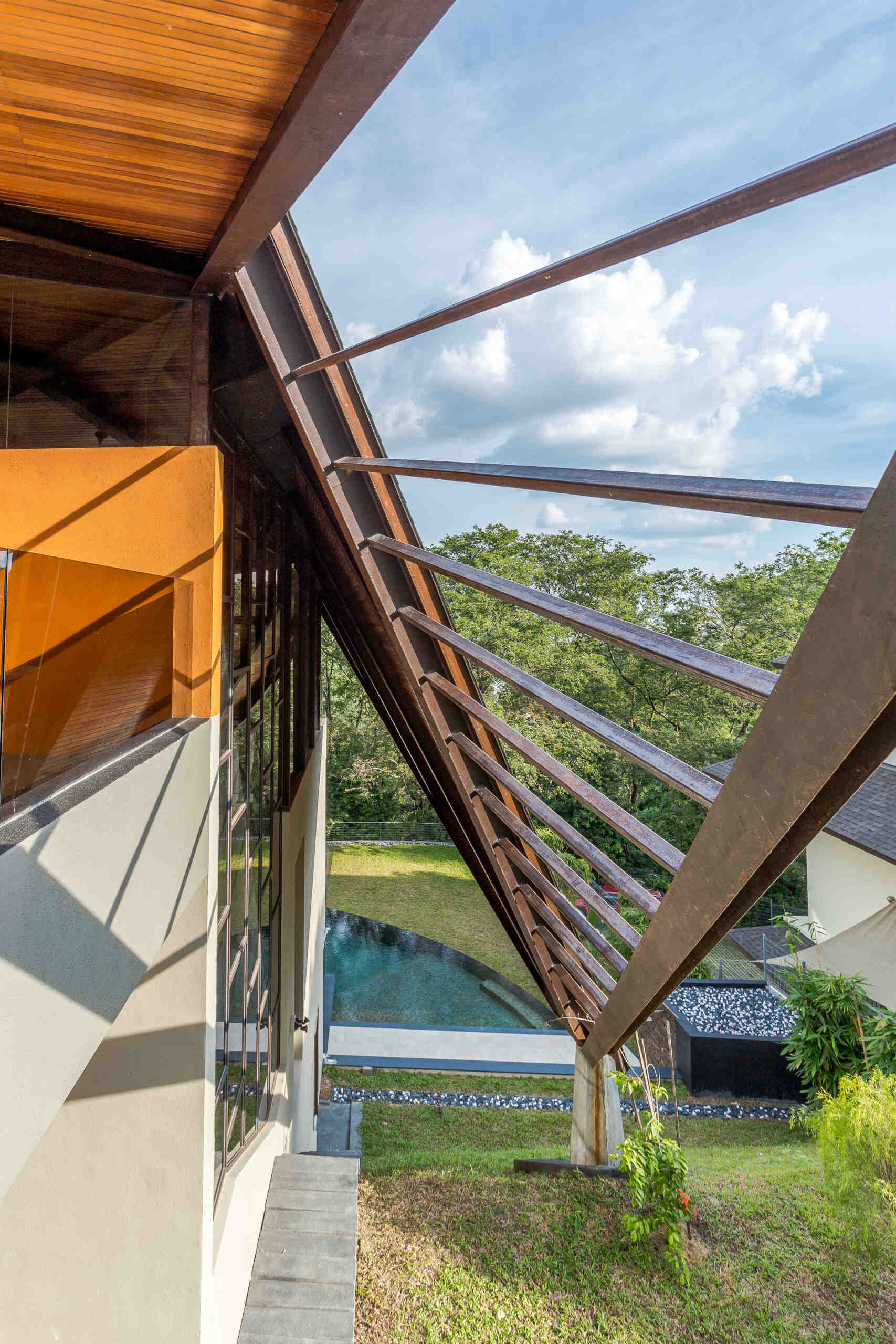 A dramatic hillside home in Kuala Lumpur designed by MJ Kanny Architect, featuring a floating timber-lined canopy roof, exposed steel beams and jungle-inspired architecture cascading down a steep slope.