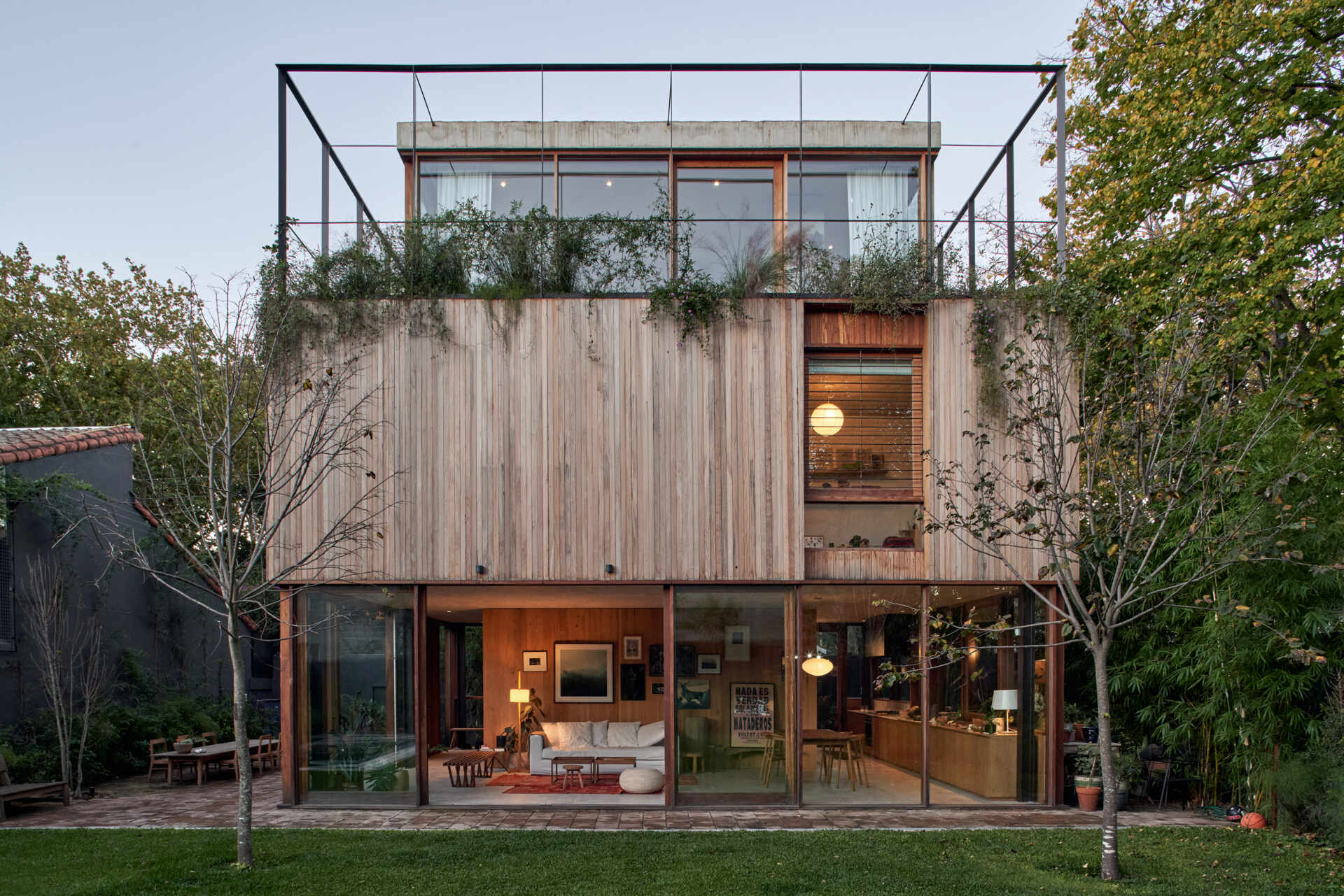 A modern home in Vicente López designed by Estudio de Ana Smud opens fully to its garden, with glass walls below and warm wood volumes above.