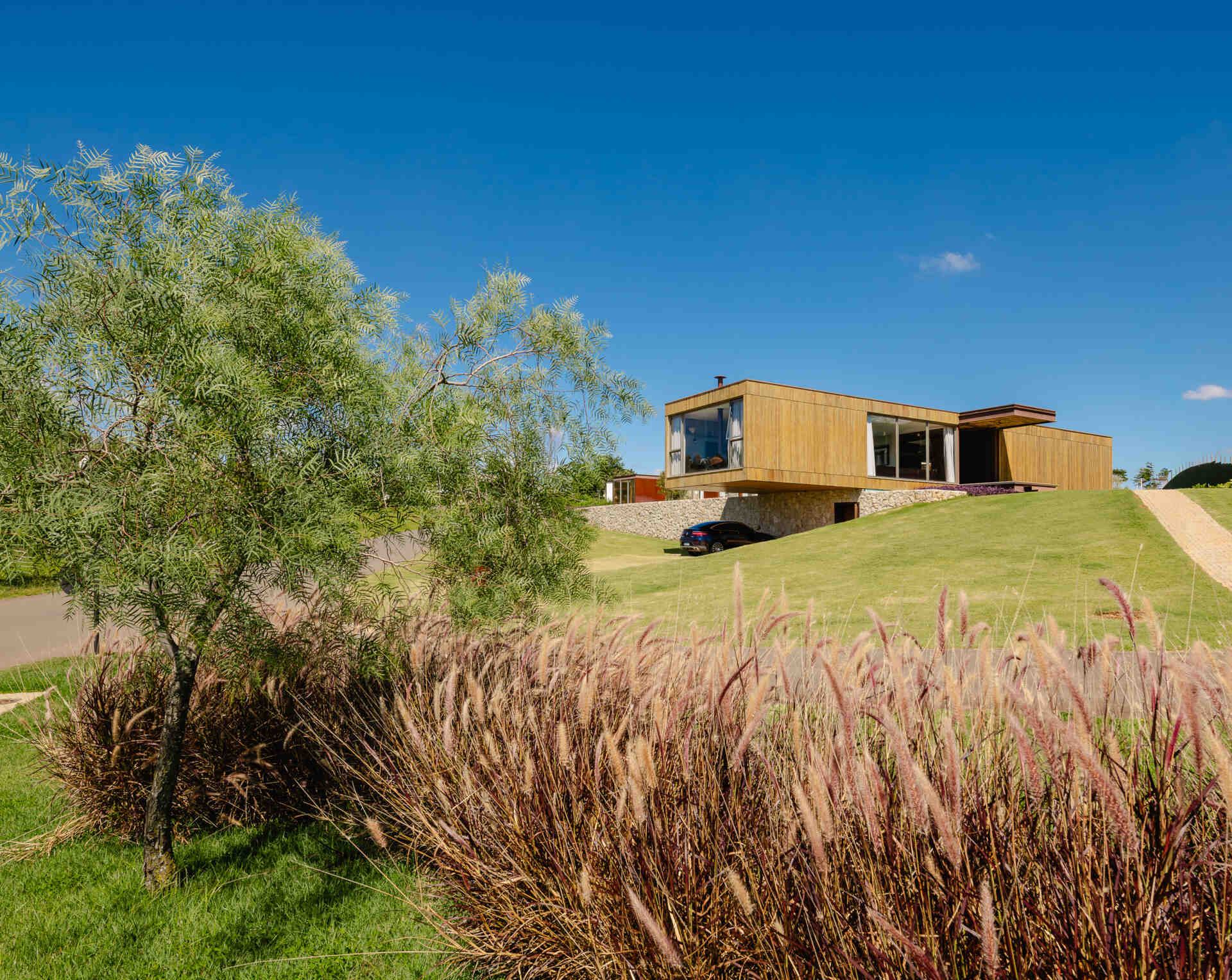 Stone walls, vertical timber slats, and lightweight steel construction give Casa Themis a warm contemporary look while helping the home blend naturally into the Brazilian landscape.