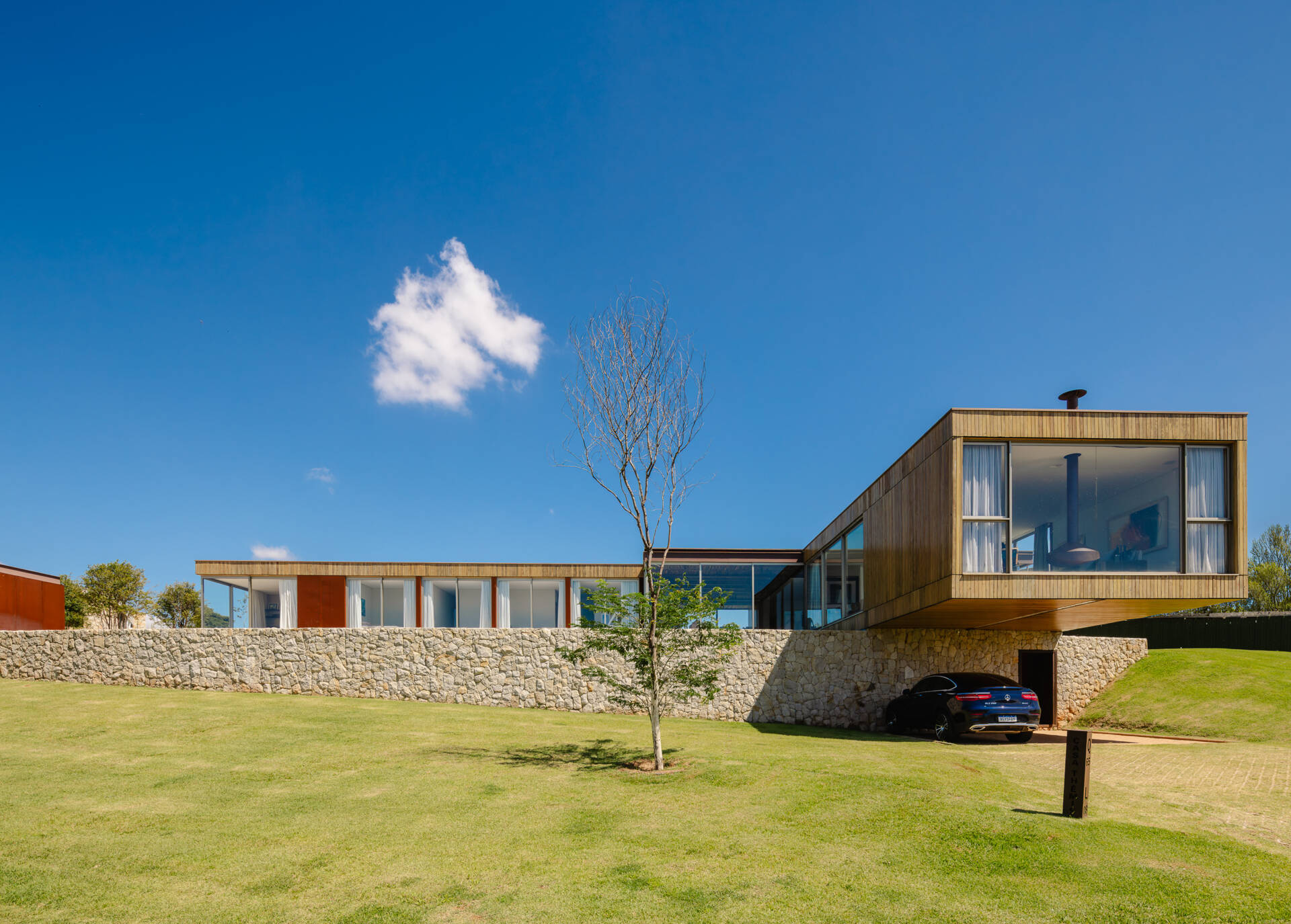 Stone walls, vertical timber slats, and lightweight steel construction give Casa Themis a warm contemporary look while helping the home blend naturally into the Brazilian landscape.