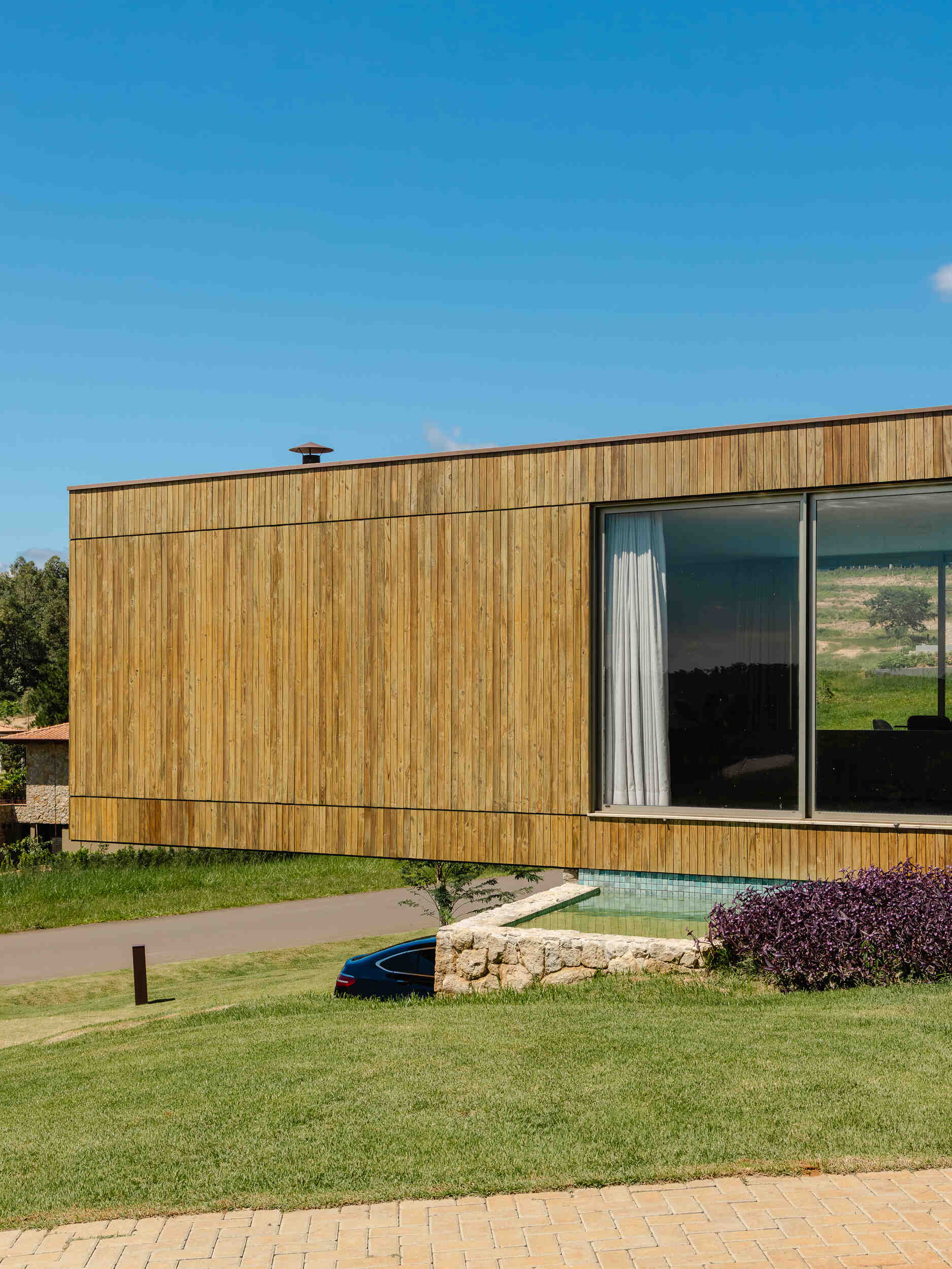 Stone walls, vertical timber slats, and lightweight steel construction give Casa Themis a warm contemporary look while helping the home blend naturally into the Brazilian landscape.