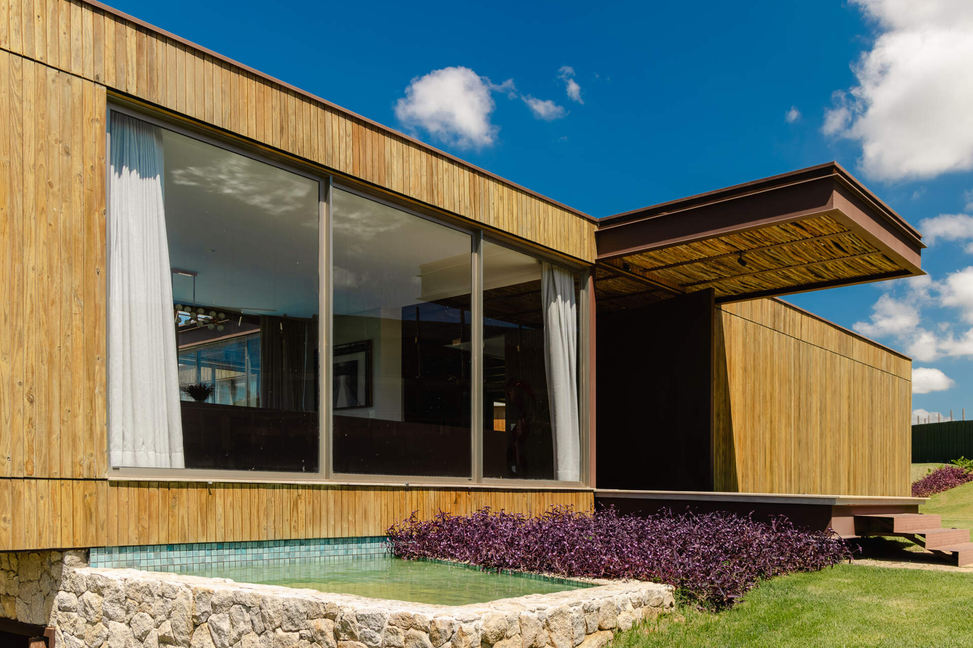 Stone walls, vertical timber slats, and lightweight steel construction give Casa Themis a warm contemporary look while helping the home blend naturally into the Brazilian landscape.