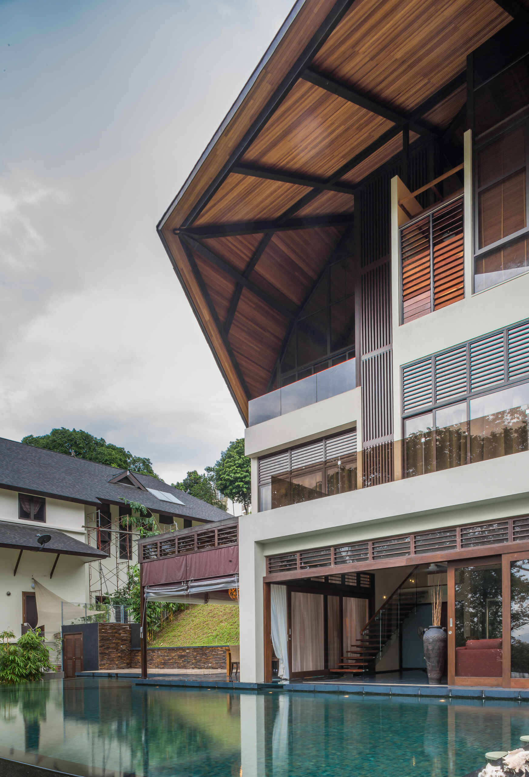 This tropical hillside pool in Kuala Lumpur is surrounded by dense greenery, shaded outdoor spaces and a floating timber canopy that blends into the jungle landscape.