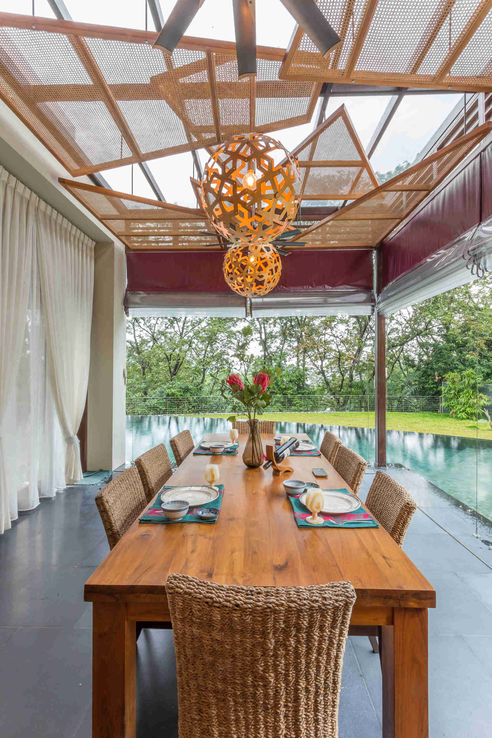 The dining area, located by the pool, continues the home’s open architectural language, where geometric rattan screens provide a shading element.