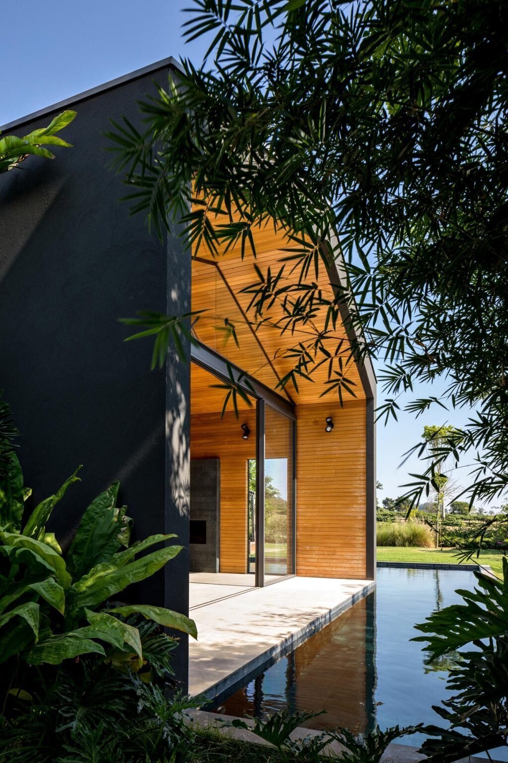 A bold black exterior contrasts with lush surroundings, framing outdoor spaces and an L-shaped pool that reflects the home’s clean geometry.
