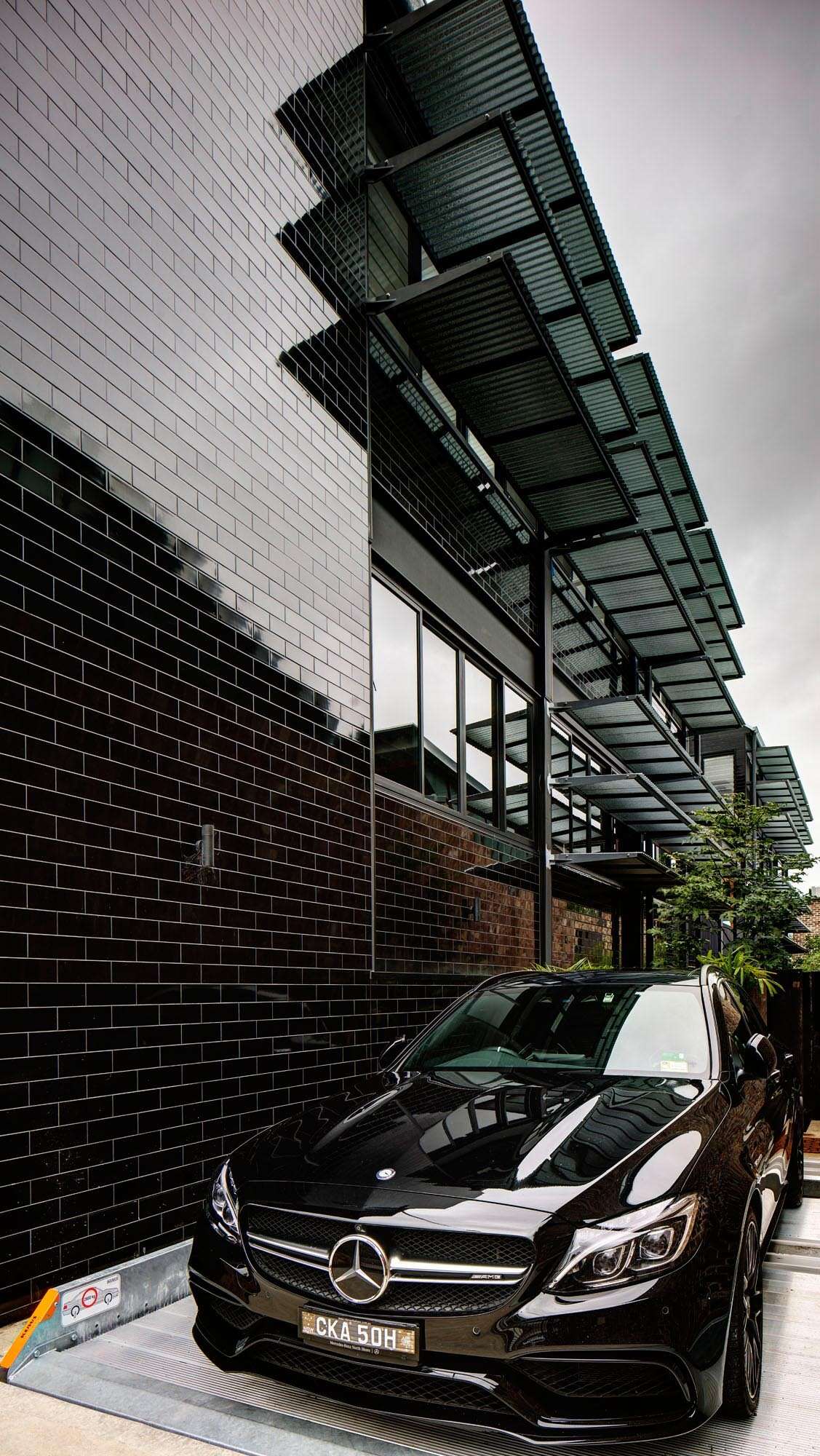 A bold glazed black tile facade wraps this Sydney warehouse conversion by Carter Williamson Architects, extending across the front and sides of the home. The reflective surface shifts with light and surrounding greenery, turning the former industrial building into a striking urban presence.