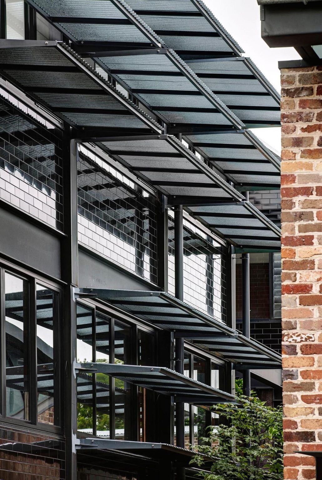 A bold glazed black tile facade wraps this Sydney warehouse conversion by Carter Williamson Architects, extending across the front and sides of the home. The reflective surface shifts with light and surrounding greenery, turning the former industrial building into a striking urban presence.