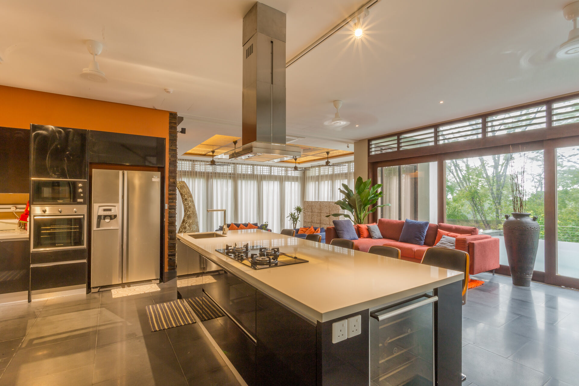 Within the flowing layout of the house, the kitchen becomes part of the larger shared living spaces instead of being hidden away. A large island provides plenty of workspace, while a painted wall and couches add a colorful accent.