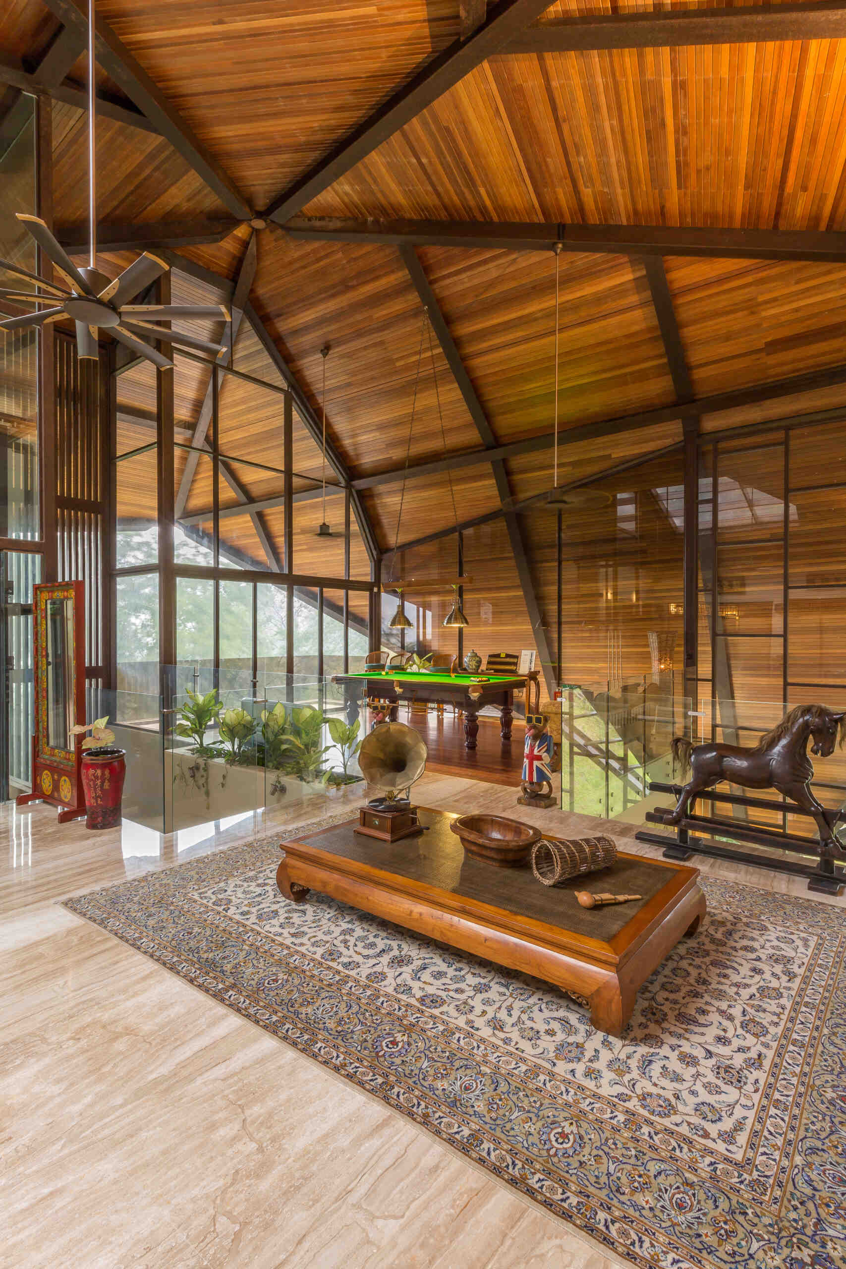This modern tropical living room sits beneath a dramatic timber canopy roof with exposed steel beams, open-air views and lush greenery surrounding every space.