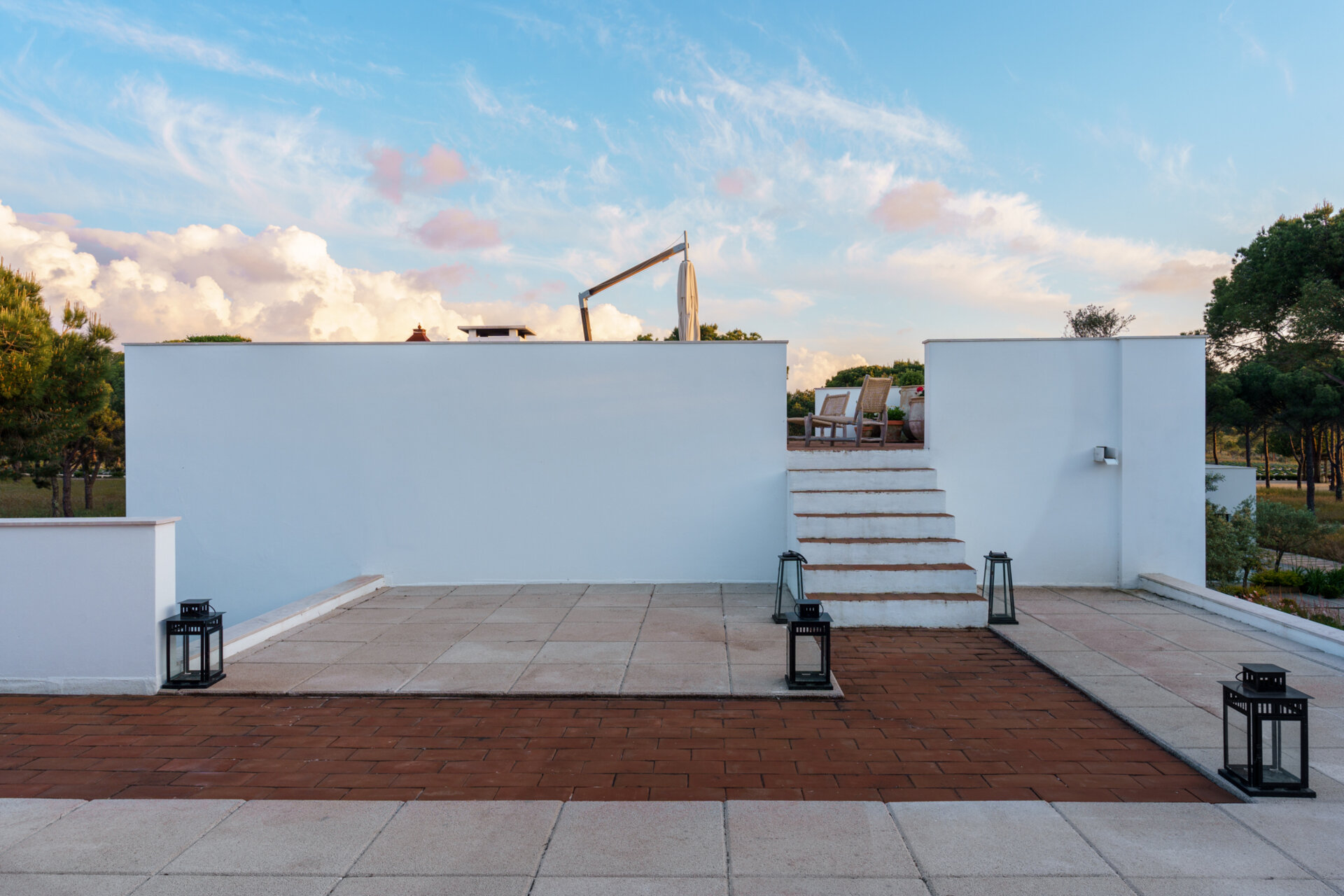 Stairs rise towards a rooftop terrace positioned above the flat roofline of the villa. This elevated outdoor space offers a completely different perspective of the surrounding pine forest.