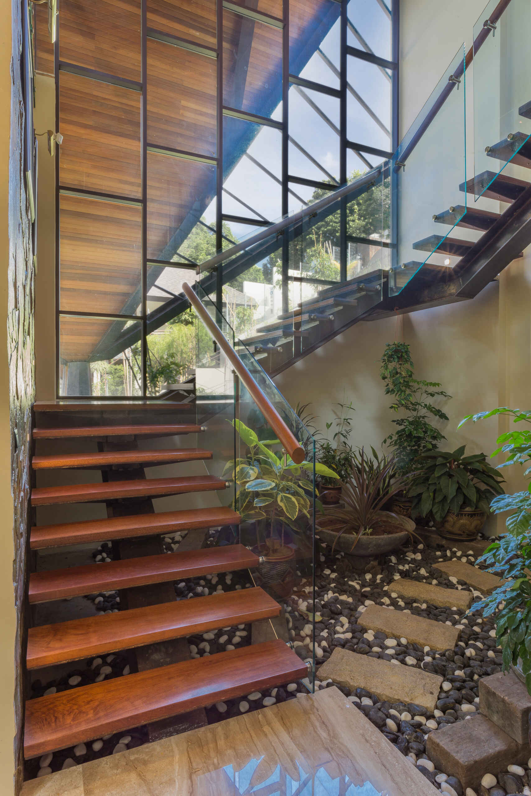 A sculptural staircase connects the cascading levels of Falanchity House, with jungle views, natural light and a timber canopy following the journey downward.