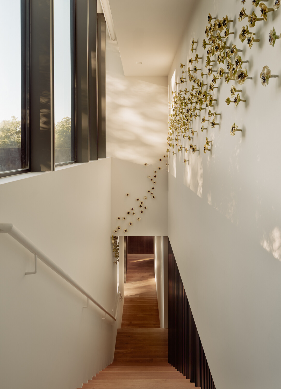 Natural light pours through tall windows in this sculptural stairwell, where warm timber treads and a striking wall installation transform circulation into a memorable architectural feature.