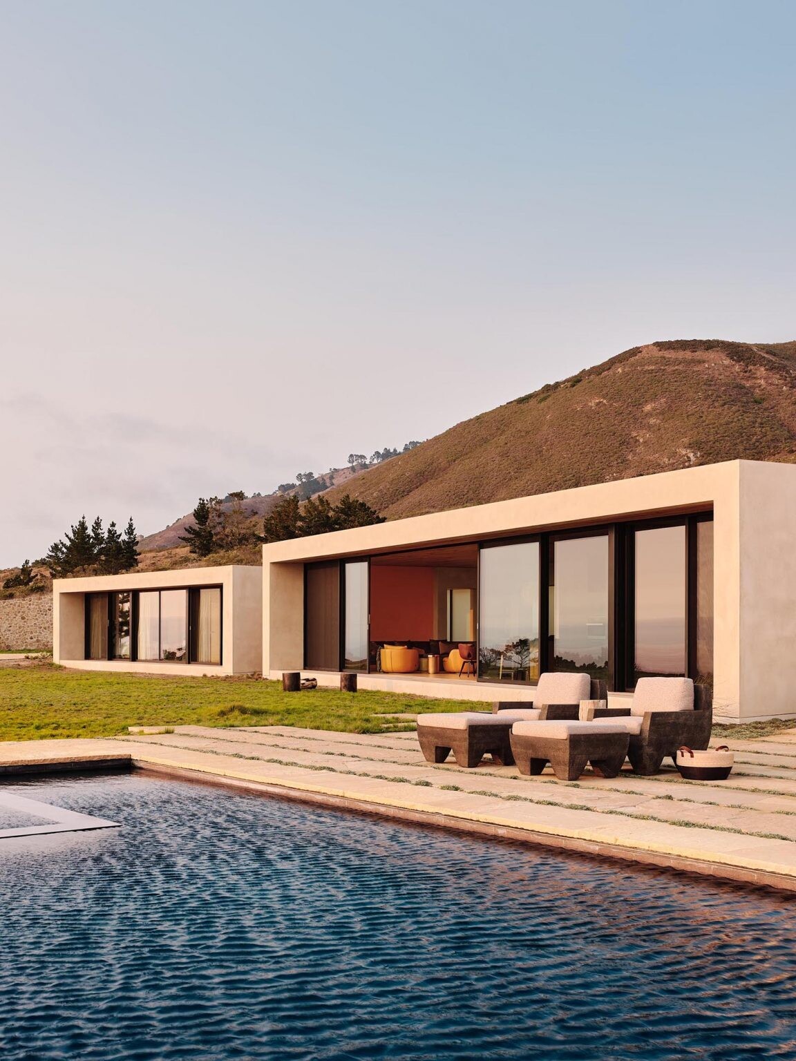 Stone walls, earth-toned concrete, and green roofs help this Big Sur home disappear into the hillside while floor-to-ceiling glass opens every space toward the Pacific Ocean.