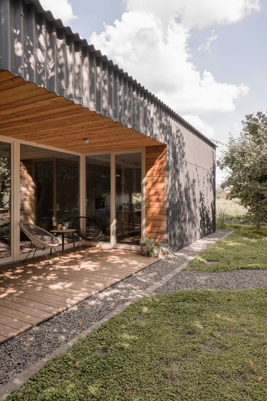 Larch wood-lined alcoves add warmth to this black modern home, creating inviting outdoor spaces that open directly toward the walnut grove.