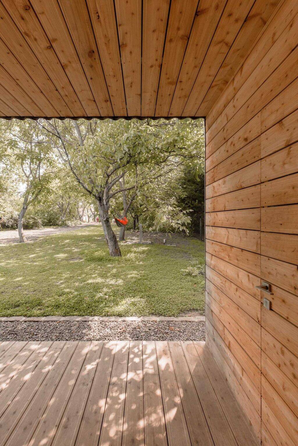 Larch wood-lined alcoves add warmth to this black modern home, creating inviting outdoor spaces that open directly toward the walnut grove.