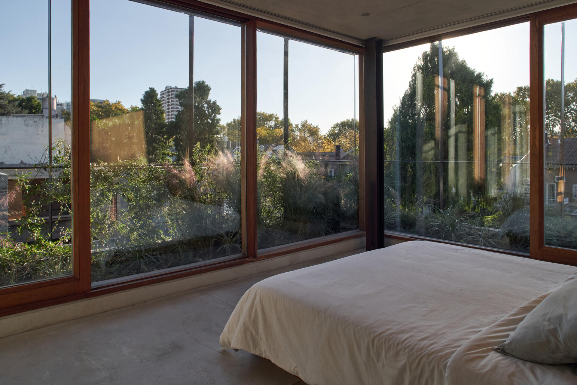 A bedroom lined with floor-to-ceiling windows brings in natural light while framing views of the surrounding trees.