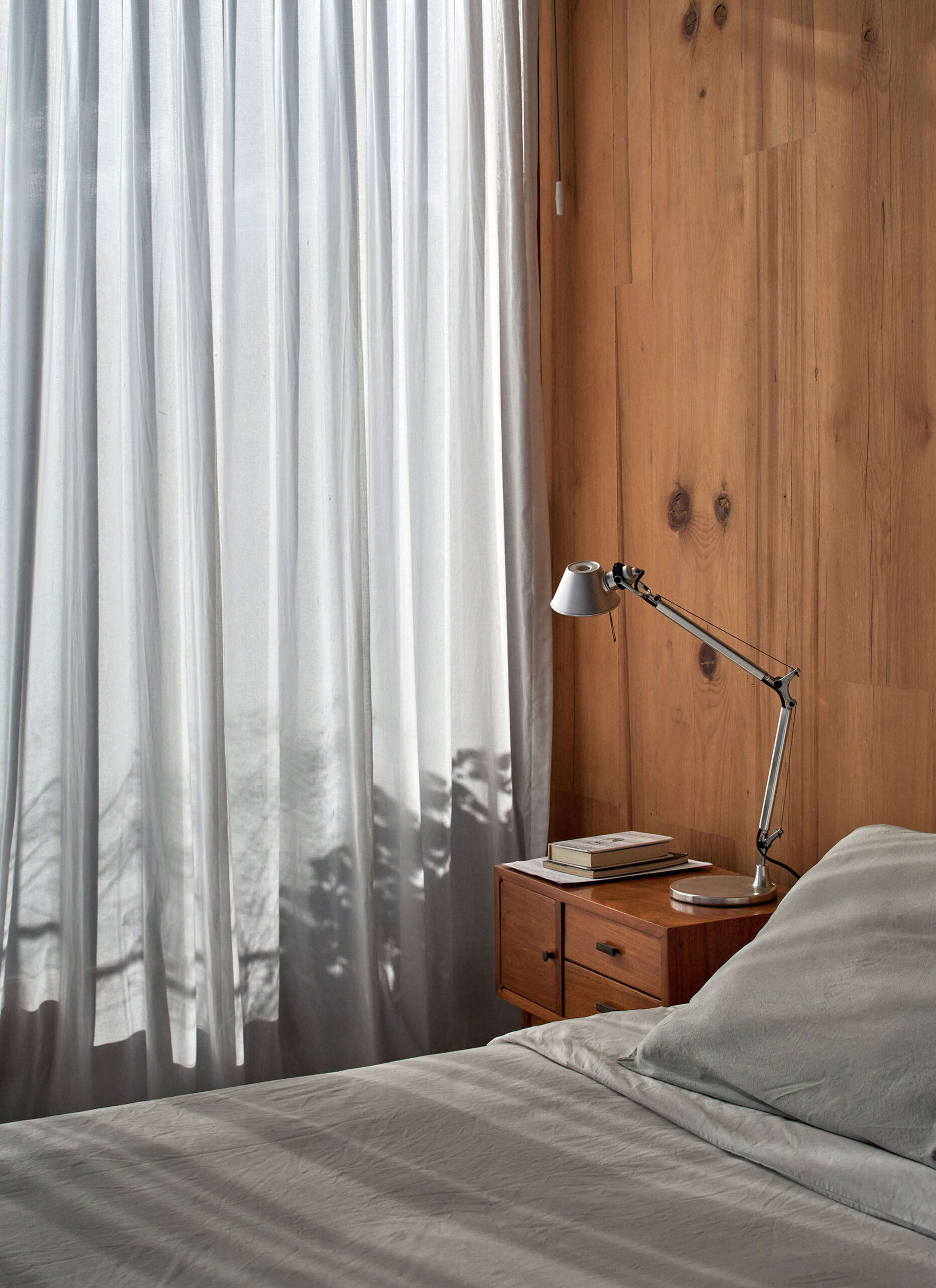 A bedroom lined with floor-to-ceiling windows brings in natural light while framing views of the surrounding trees.
