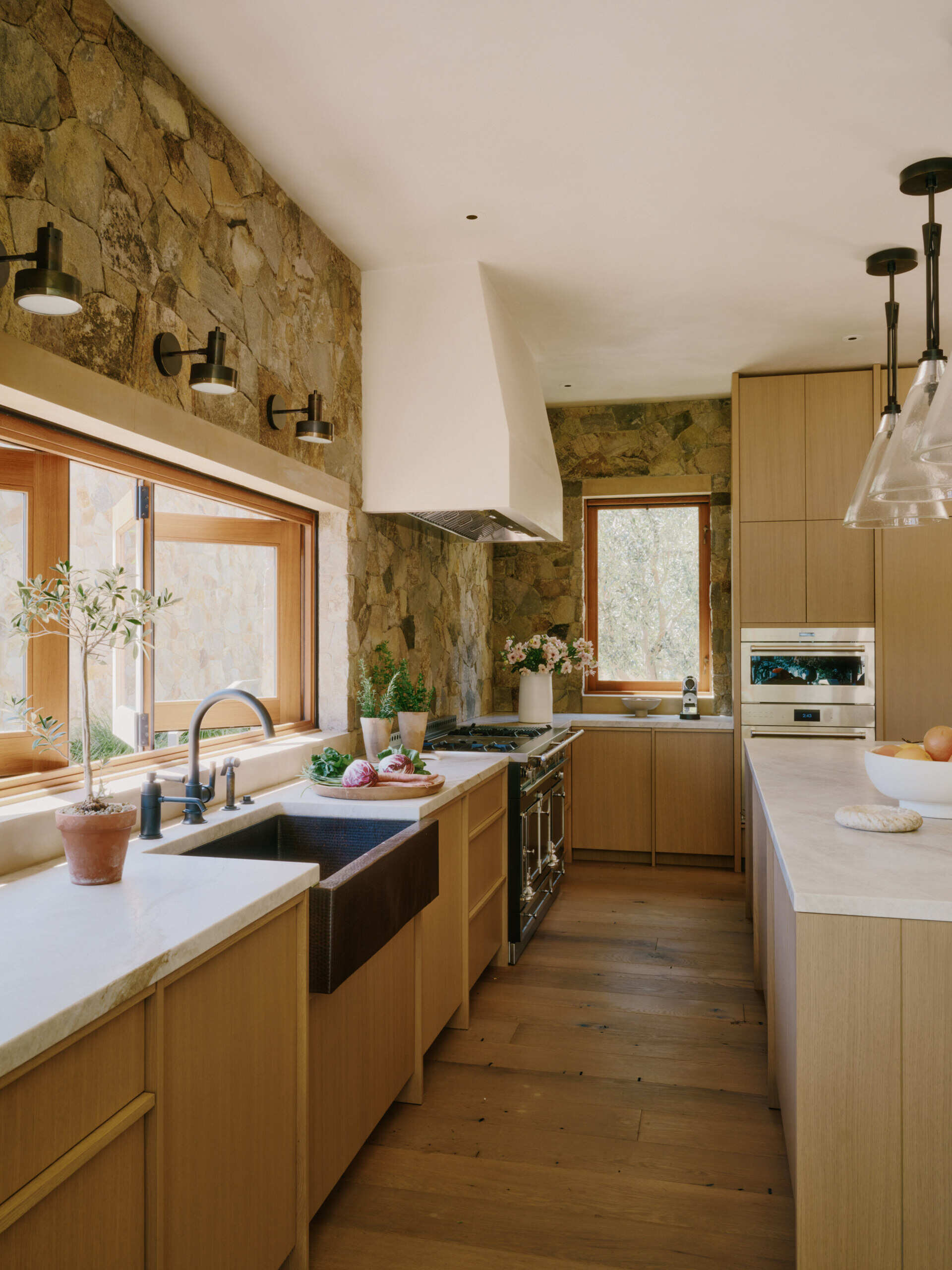 This modern kitchen combines stone surfaces, warm wood cabinetry, and natural light with seamless access to outdoor entertaining spaces.