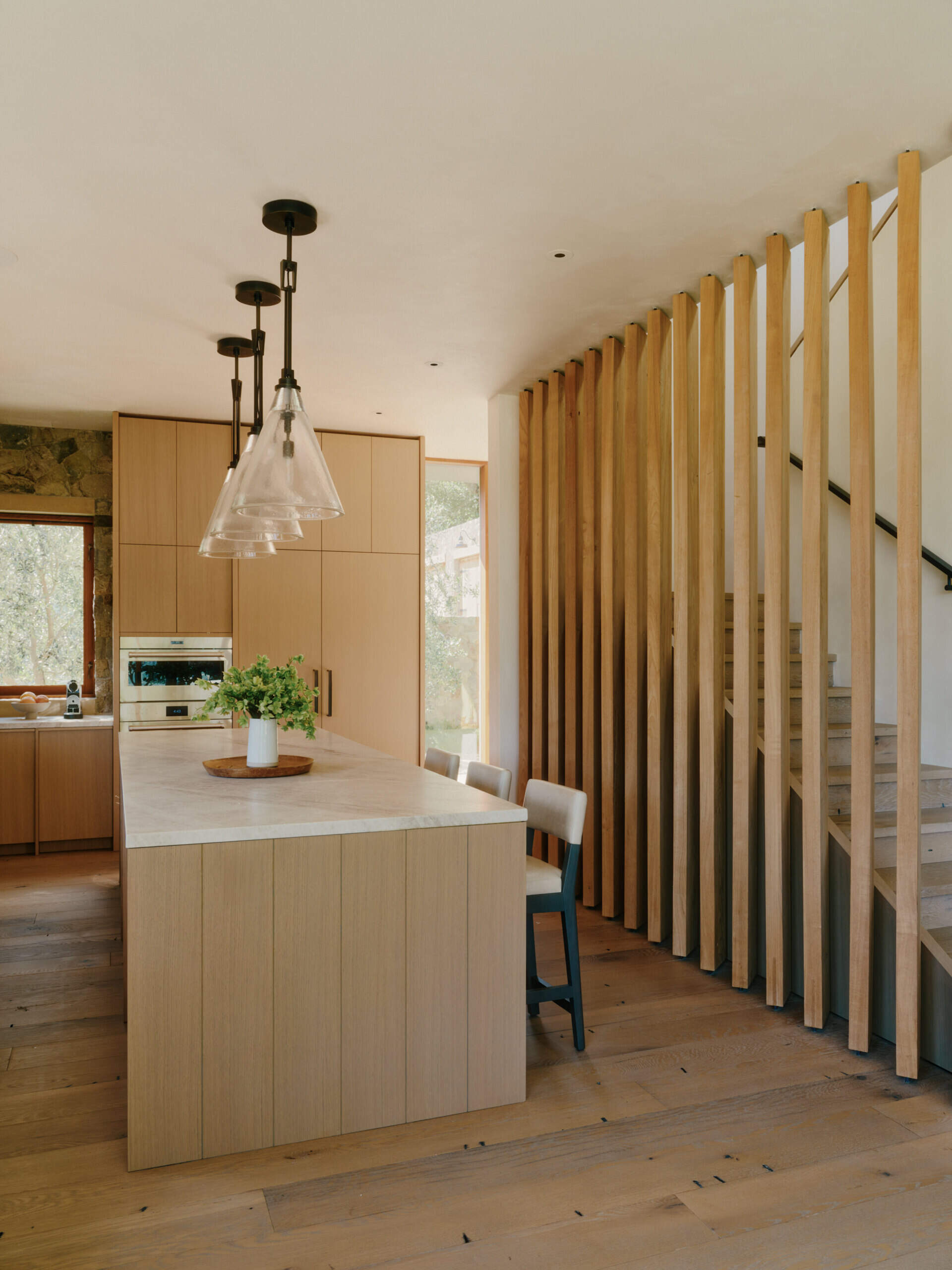 This modern kitchen combines stone surfaces, warm wood cabinetry, and natural light with seamless access to outdoor entertaining spaces.