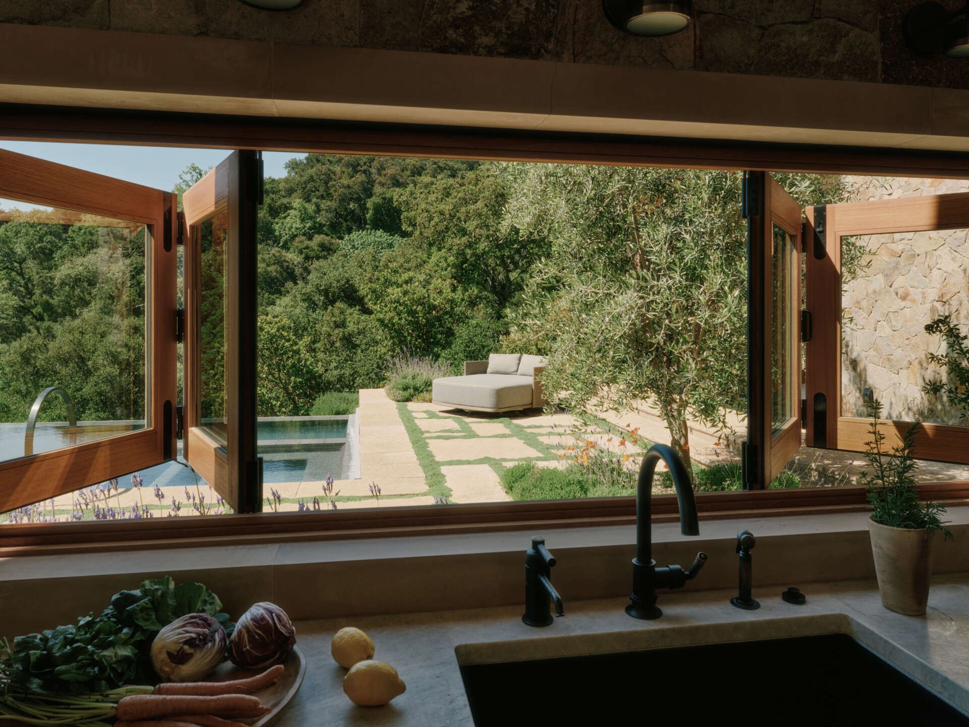This modern kitchen combines stone surfaces, warm wood cabinetry, and natural light with seamless access to outdoor entertaining spaces.