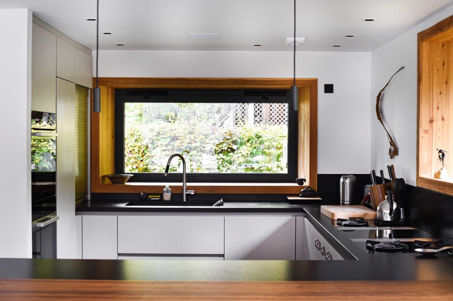 A modern kitchen with white cabinets, black countertops, and wood framed windows.