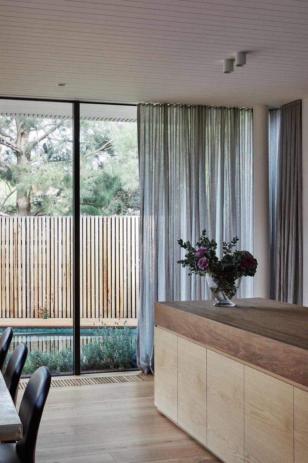 This open-plan Melbourne living space connects directly to an outdoor deck and green plunge pool through massive sliding glass doors and floor-to-ceiling windows.