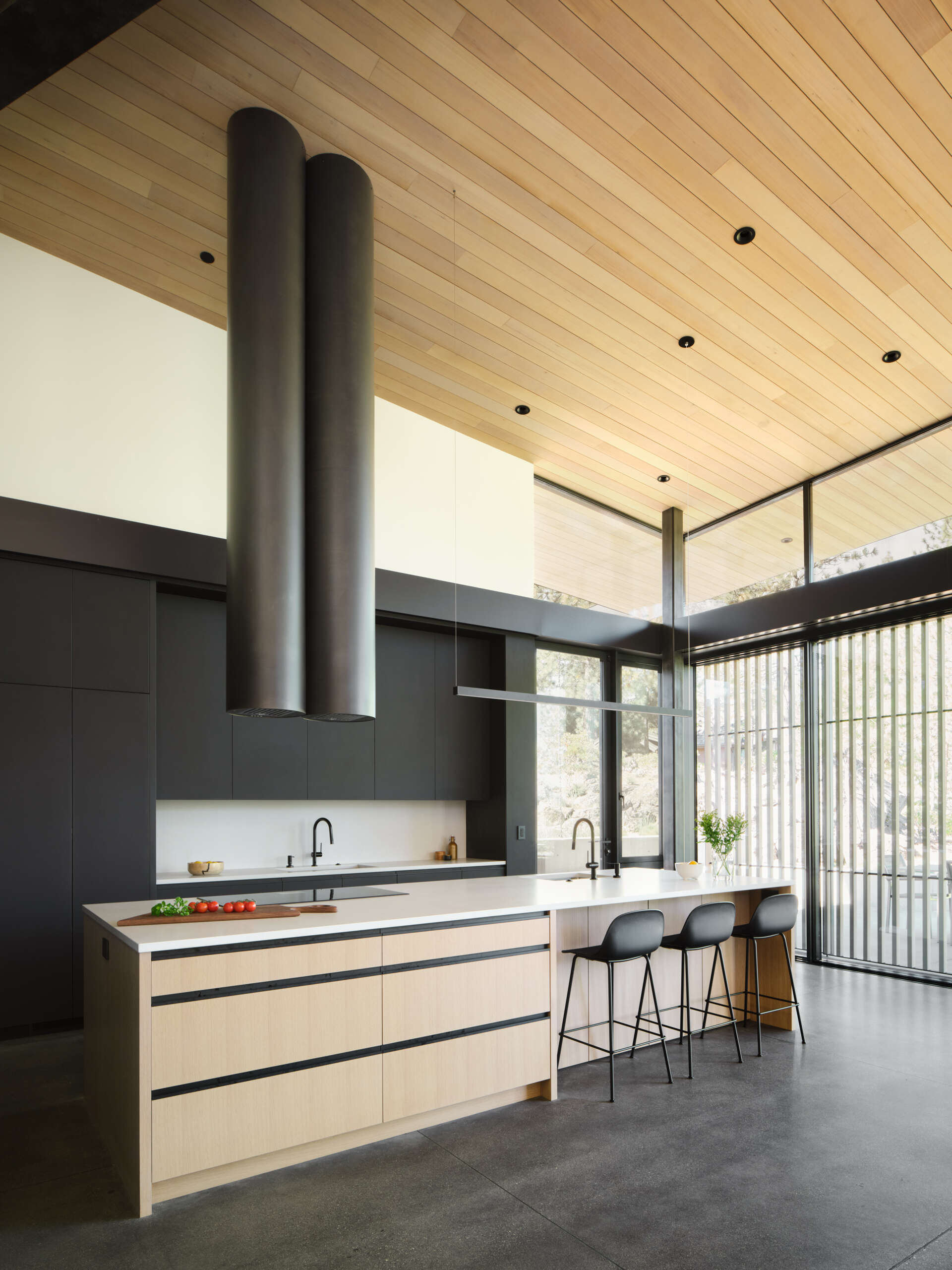 Warm wood cabinetry, concrete floors, and forest views give this modern Oregon kitchen a clean yet welcoming atmosphere.