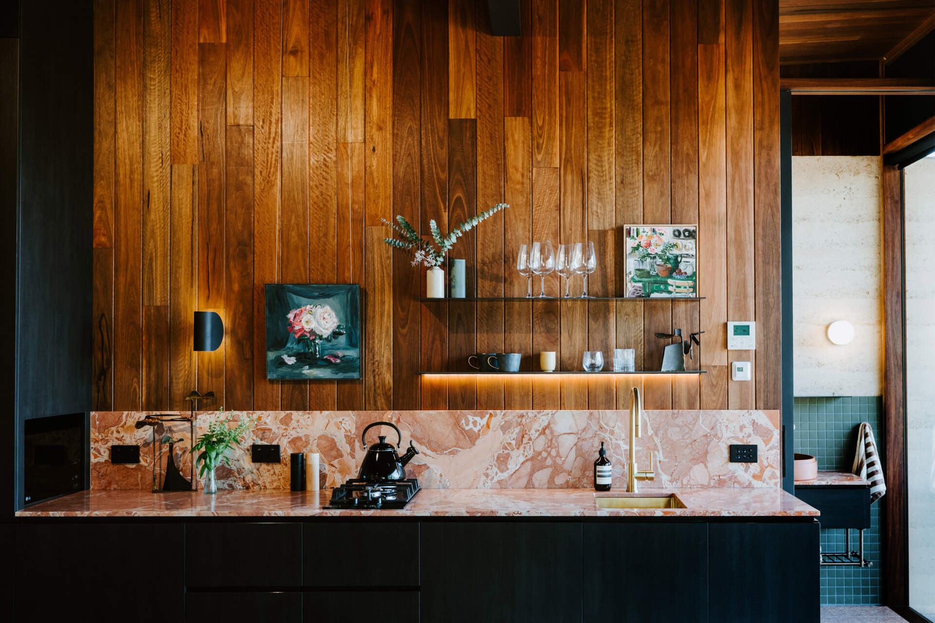 A modern kitchenette with wood walls and stone with pink tones.
