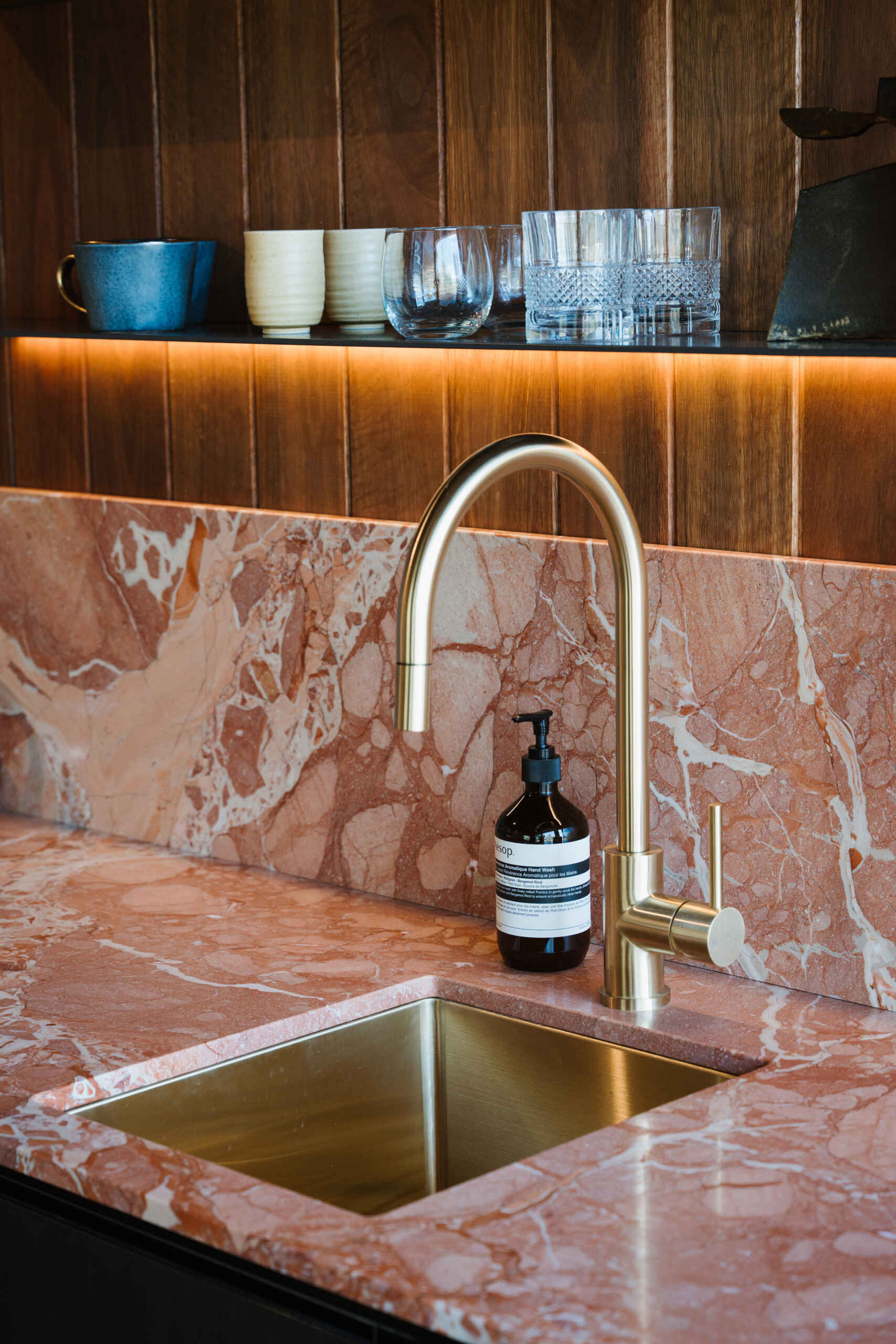 A modern kitchenette with wood walls and stone with pink tones.