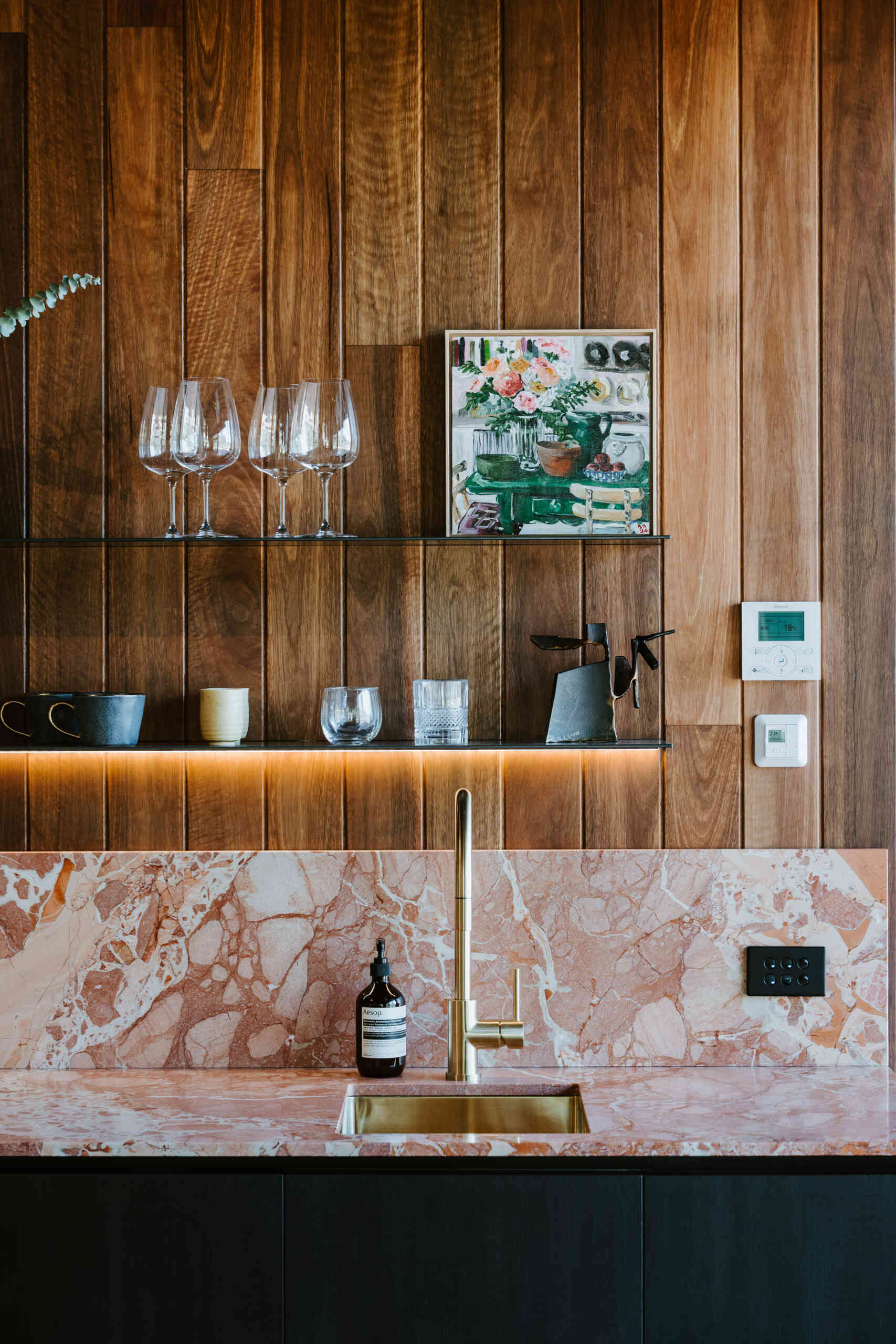 A modern kitchenette with wood walls and stone with pink tones.