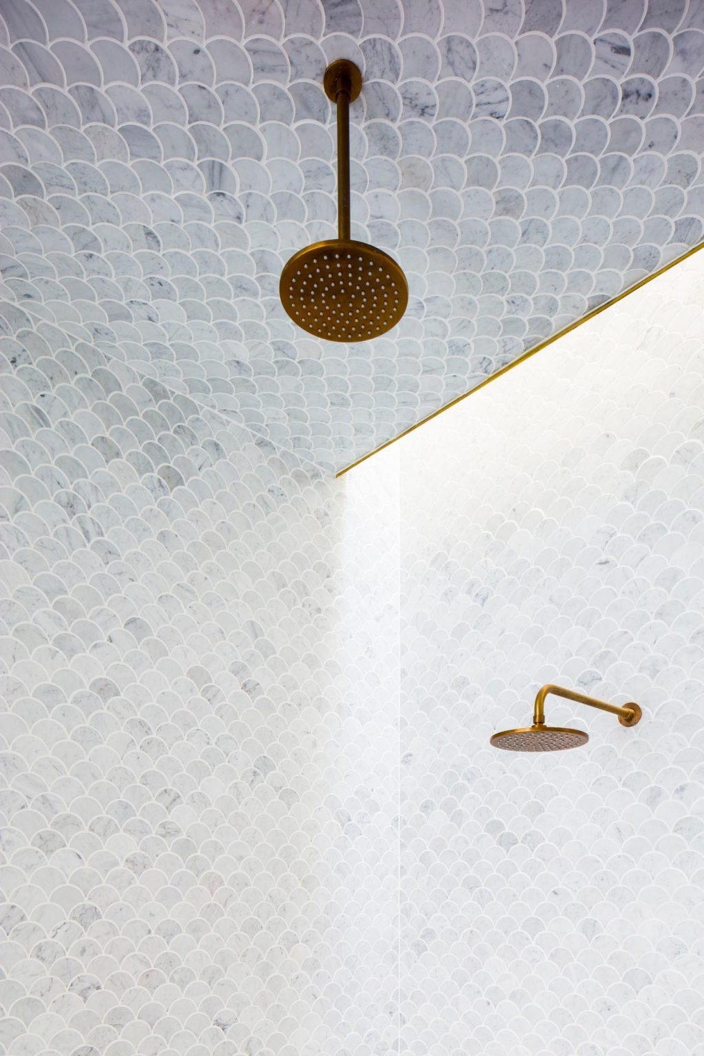 The main ensuite is wrapped in light grey fan-shaped tiles that extend across ceilings and tall walls, paired with brass fixtures that introduce warmth against the cool surface.