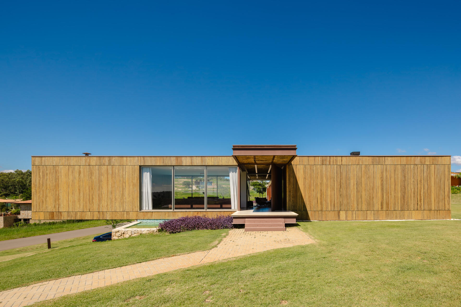 Casa Themis in Itu, Brazil transforms a sloping countryside site into a warm modern home with stone walls, wood cladding, and expansive outdoor living spaces designed for weekends with family and friends.
