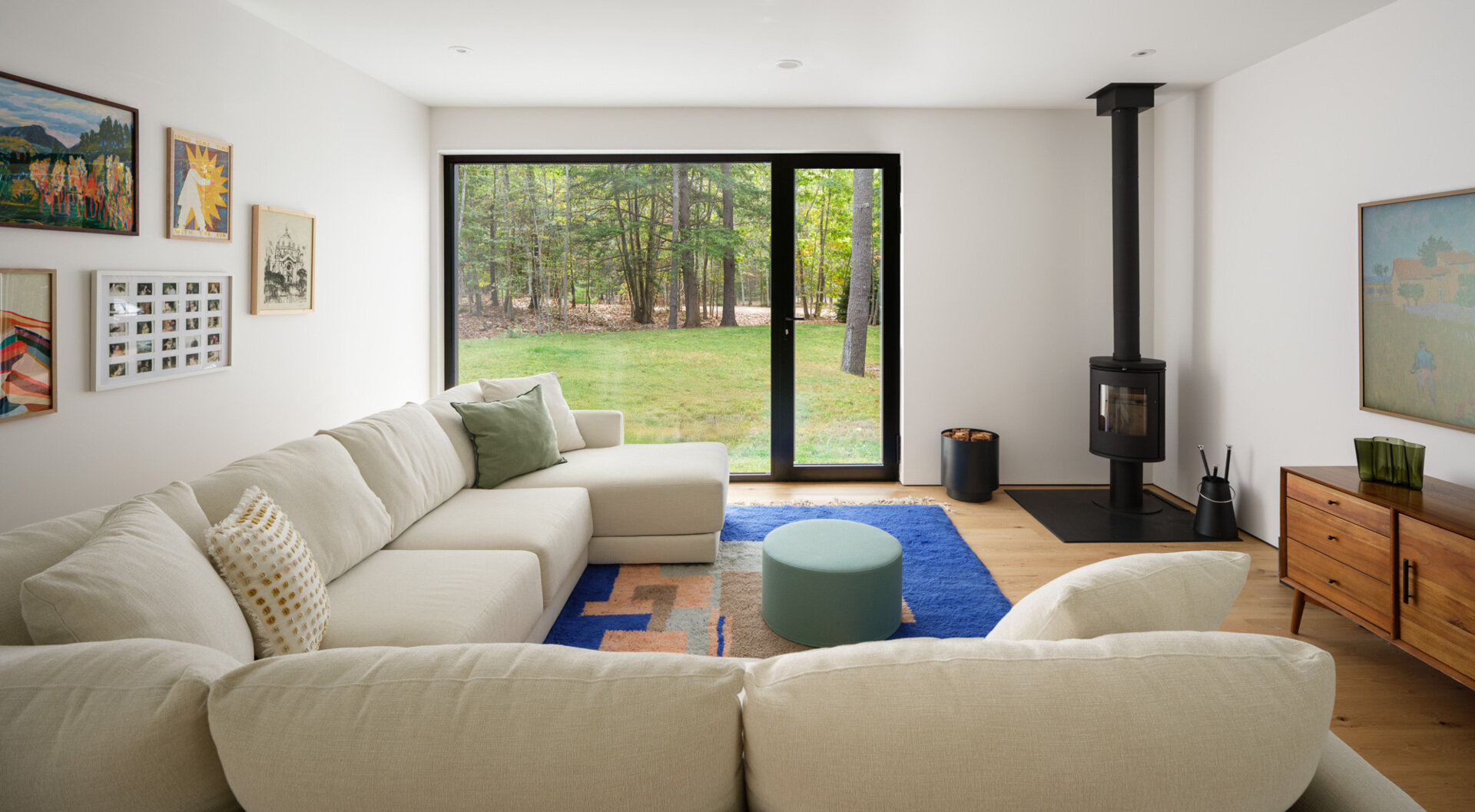 Floor-to-ceiling windows and pale wood interiors fill this modern living room with natural light and forest views.