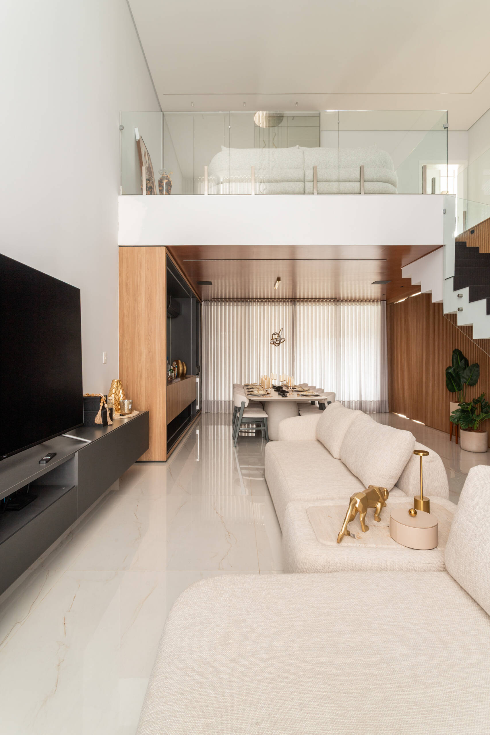 A dramatic double-height living room in Casa R|L combines exposed concrete, warm wood finishes, and sculptural structural elements in this contemporary Brazilian home.