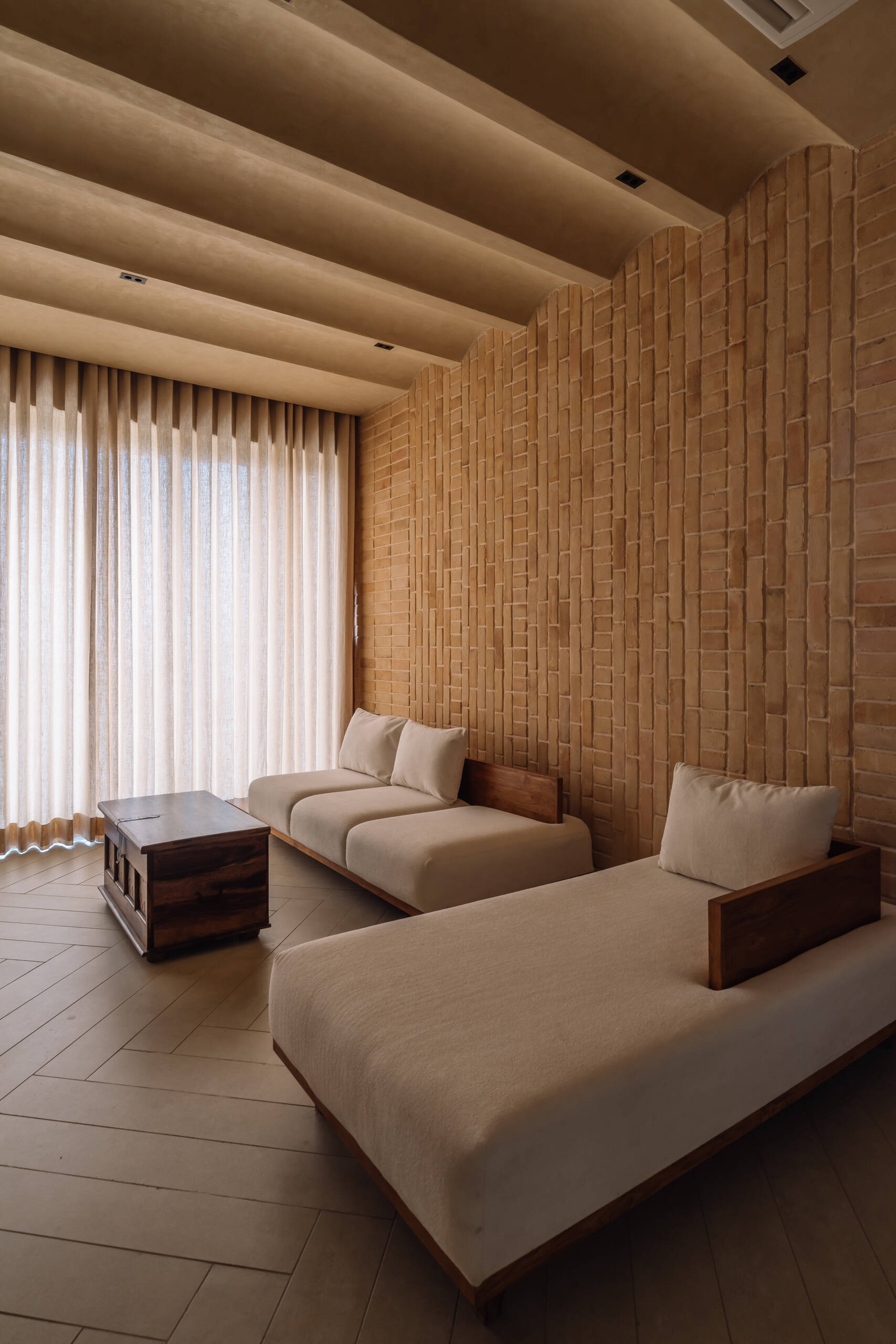 Exposed brick walls and sculptural arches give this Ahmedabad living room a warm minimalist atmosphere filled with texture, light, and soft architectural forms.