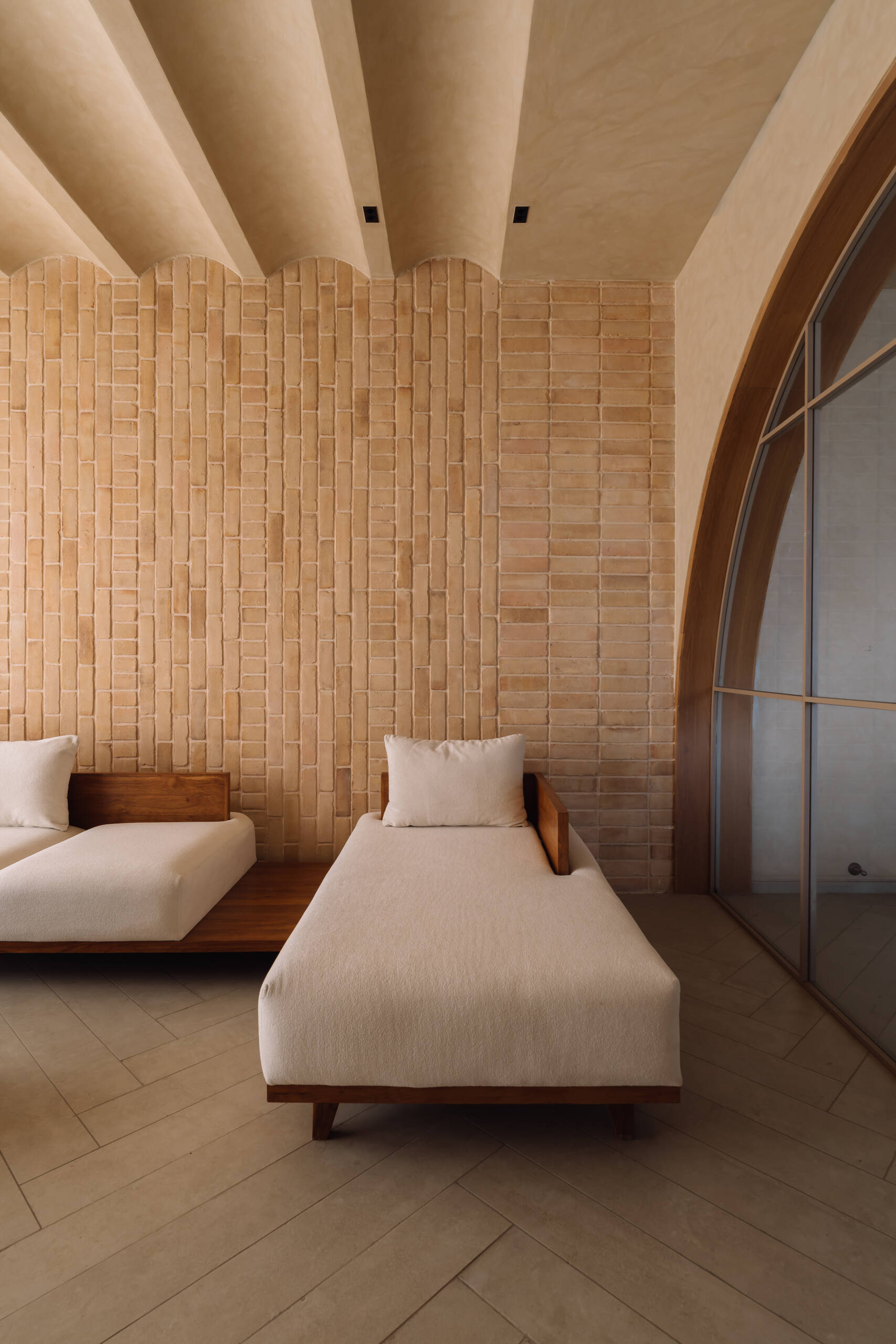 Exposed brick walls and sculptural arches give this Ahmedabad living room a warm minimalist atmosphere filled with texture, light, and soft architectural forms.
