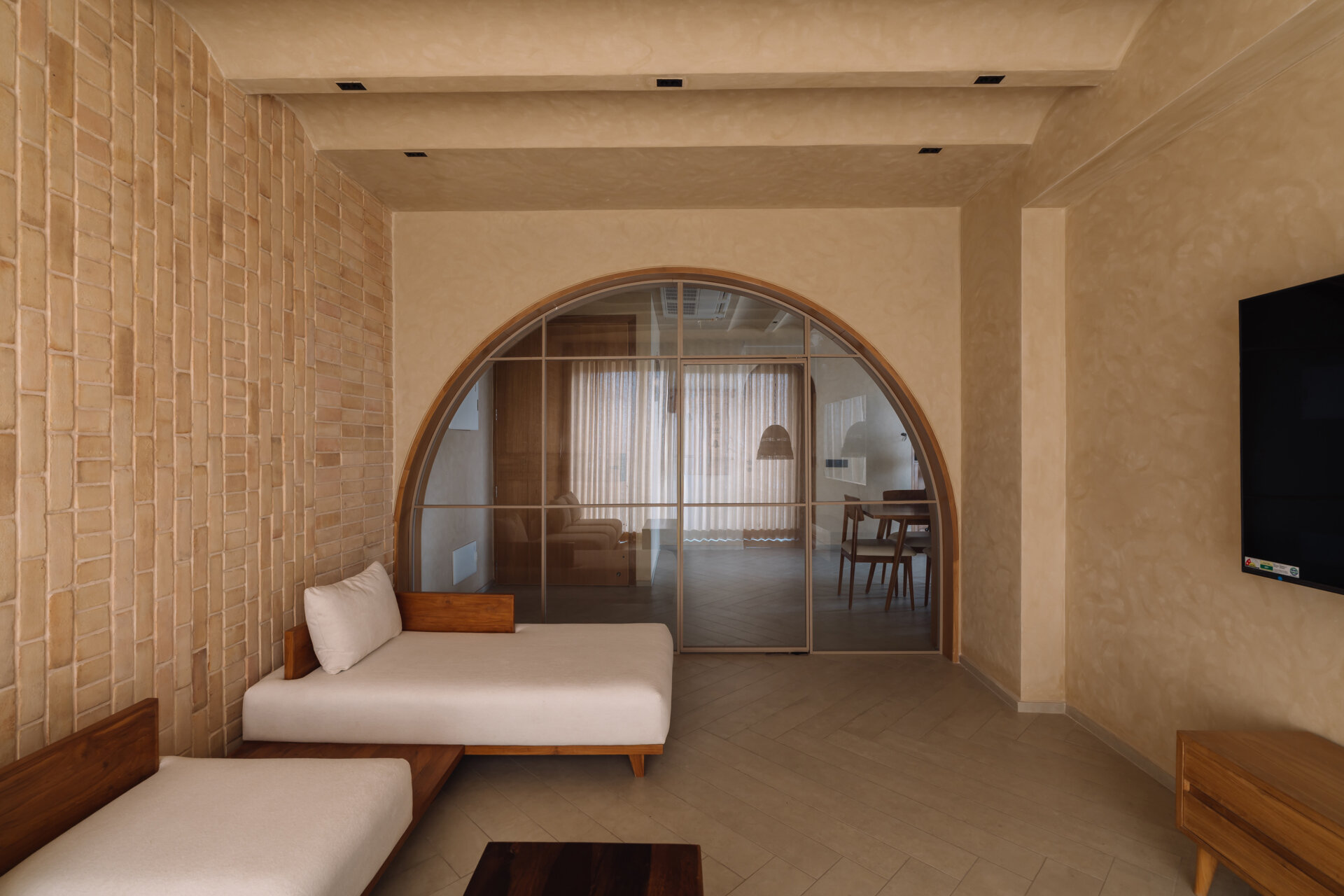 Exposed brick walls and sculptural arches give this Ahmedabad living room a warm minimalist atmosphere filled with texture, light, and soft architectural forms.