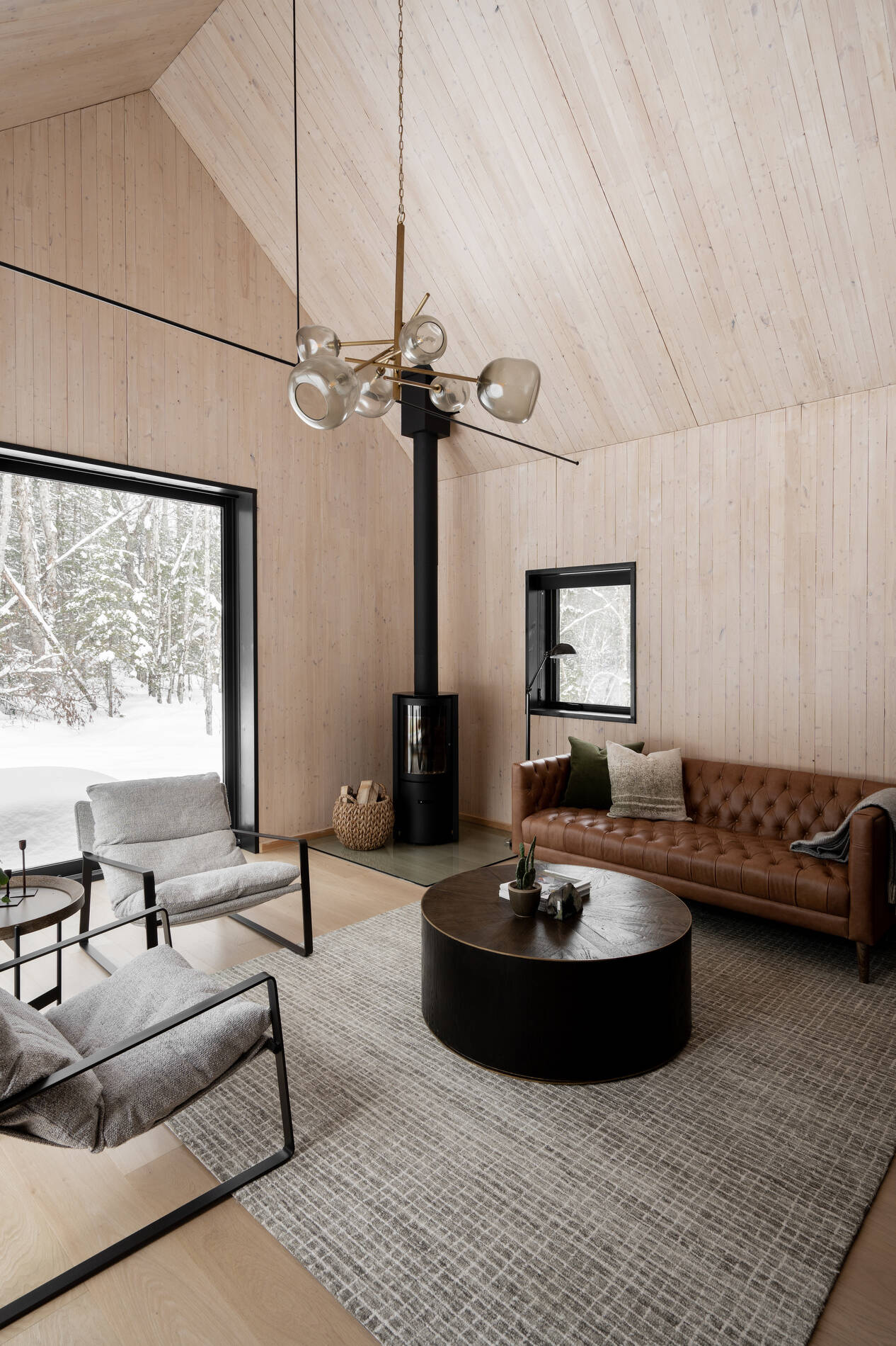 A modern living room with a fireplace in the corner and large windows that look out onto the landscape.