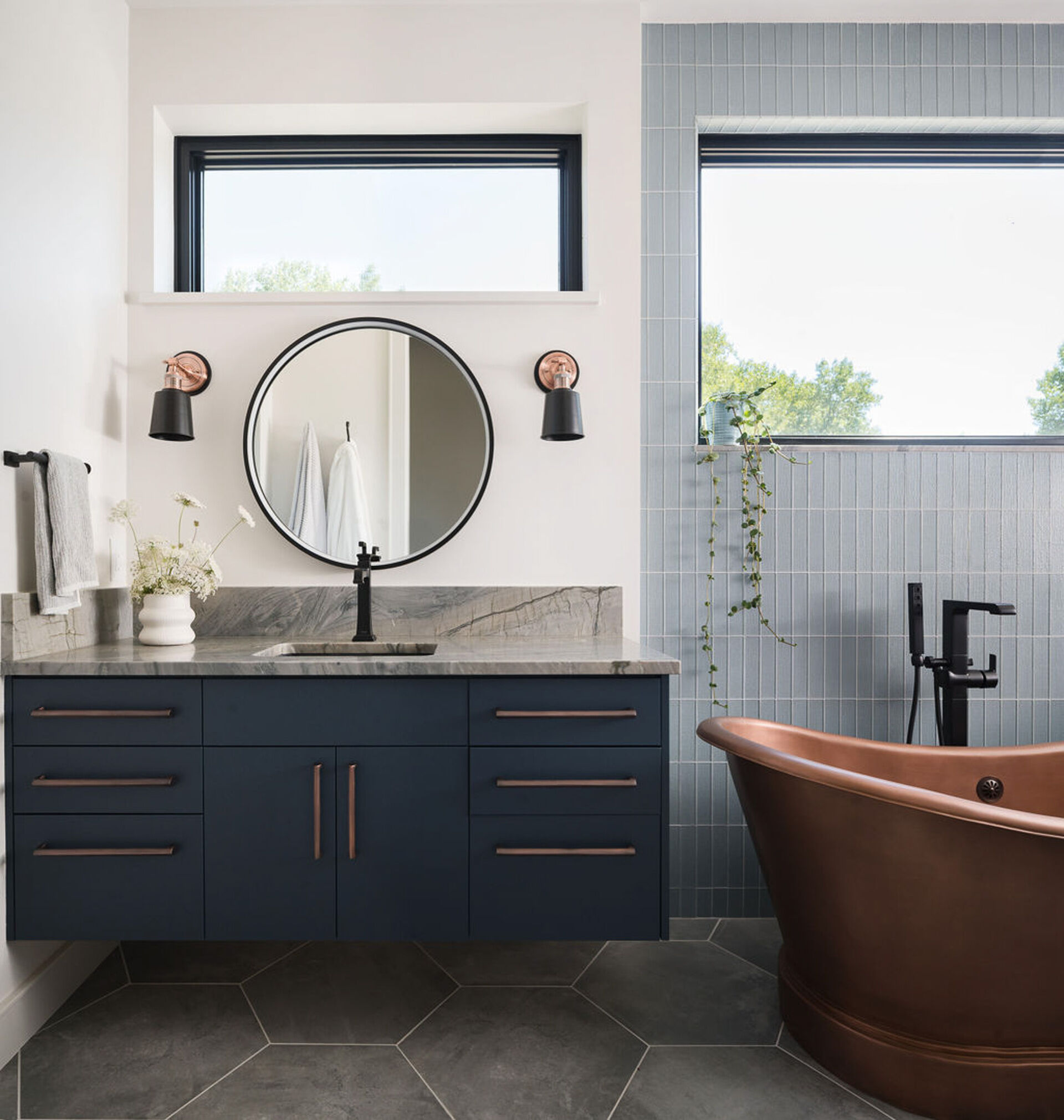 Copper accents, navy cabinetry, and soft blue tile bring warmth and contrast to this bright modern bathroom.