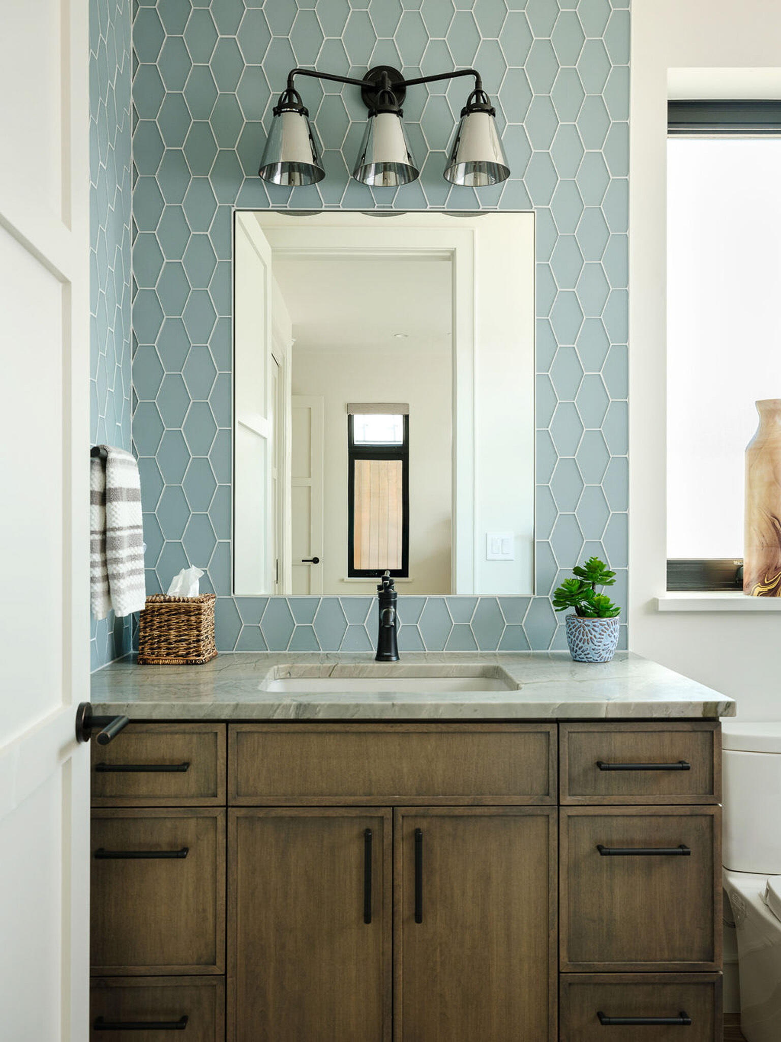 Blue hex tile, warm wood cabinetry, and matte black fixtures shape this fresh modern bathroom design.