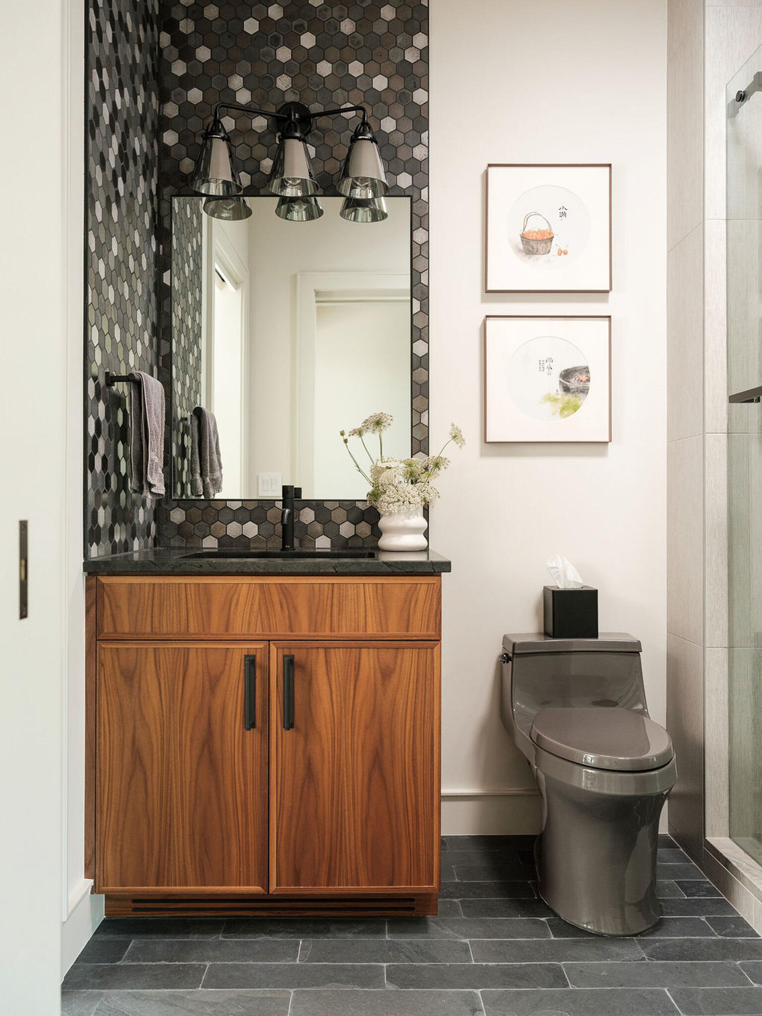 Dark hex tile and warm wood cabinetry create a refined modern bathroom with rich texture and contrast.
