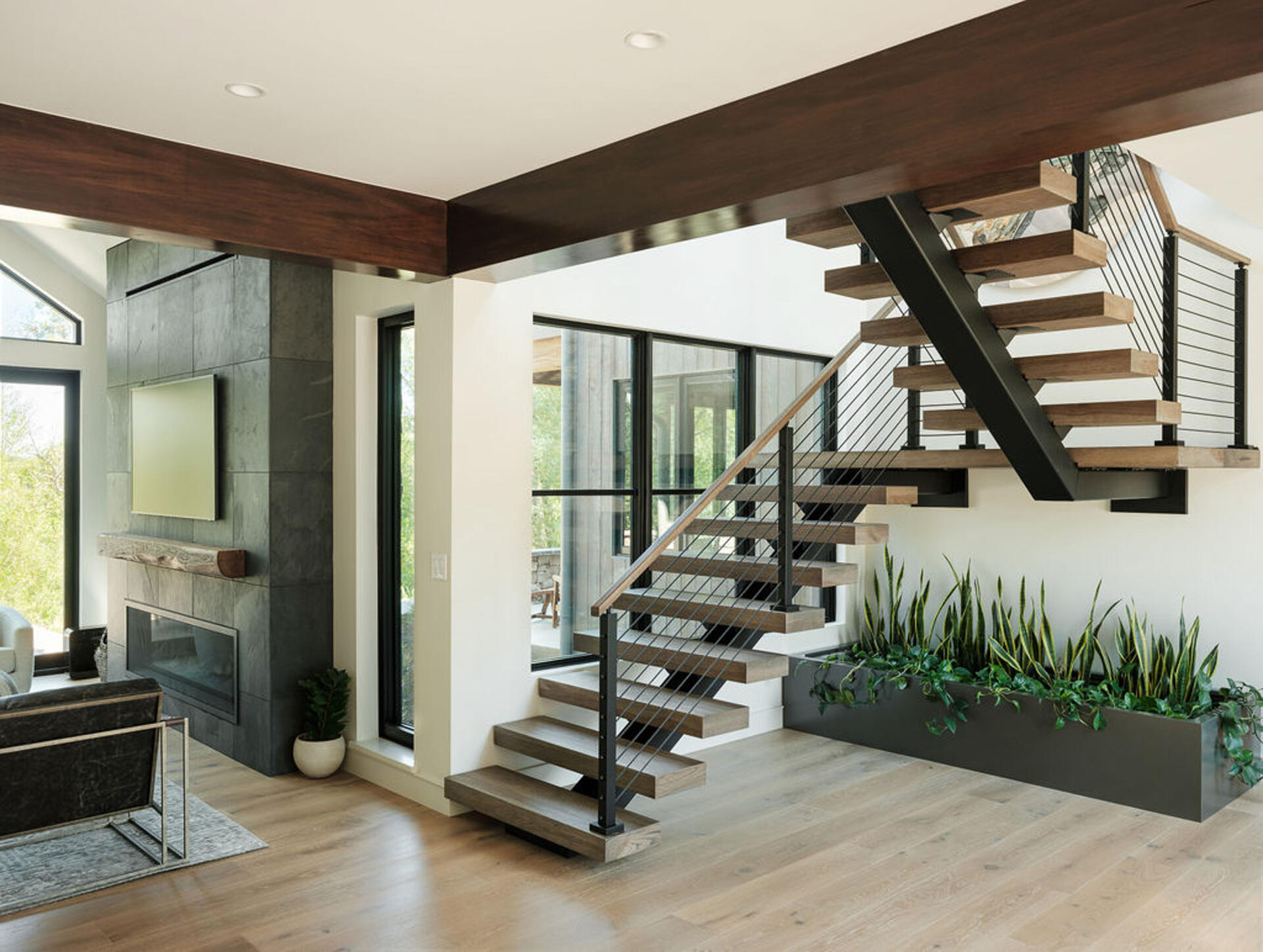 A glass stair bridge introduces transparency and openness between levels, creating a sense of suspension above the spaces below, while planter is positioned beneath the stairs, offering a natural element to the interior.