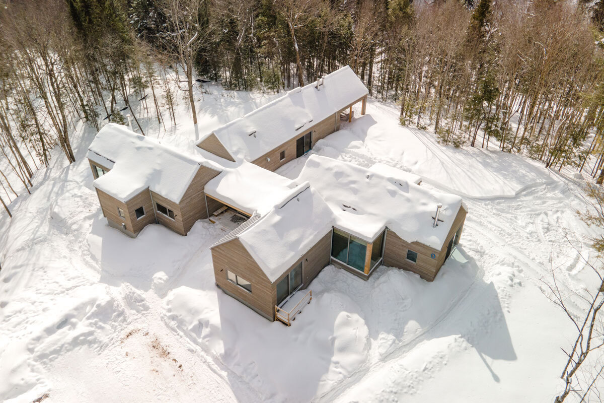 A Quebec mountain house built with cross-laminated timber, featuring gabled volumes and a pinwheel layout that blends into the surrounding landscape.
